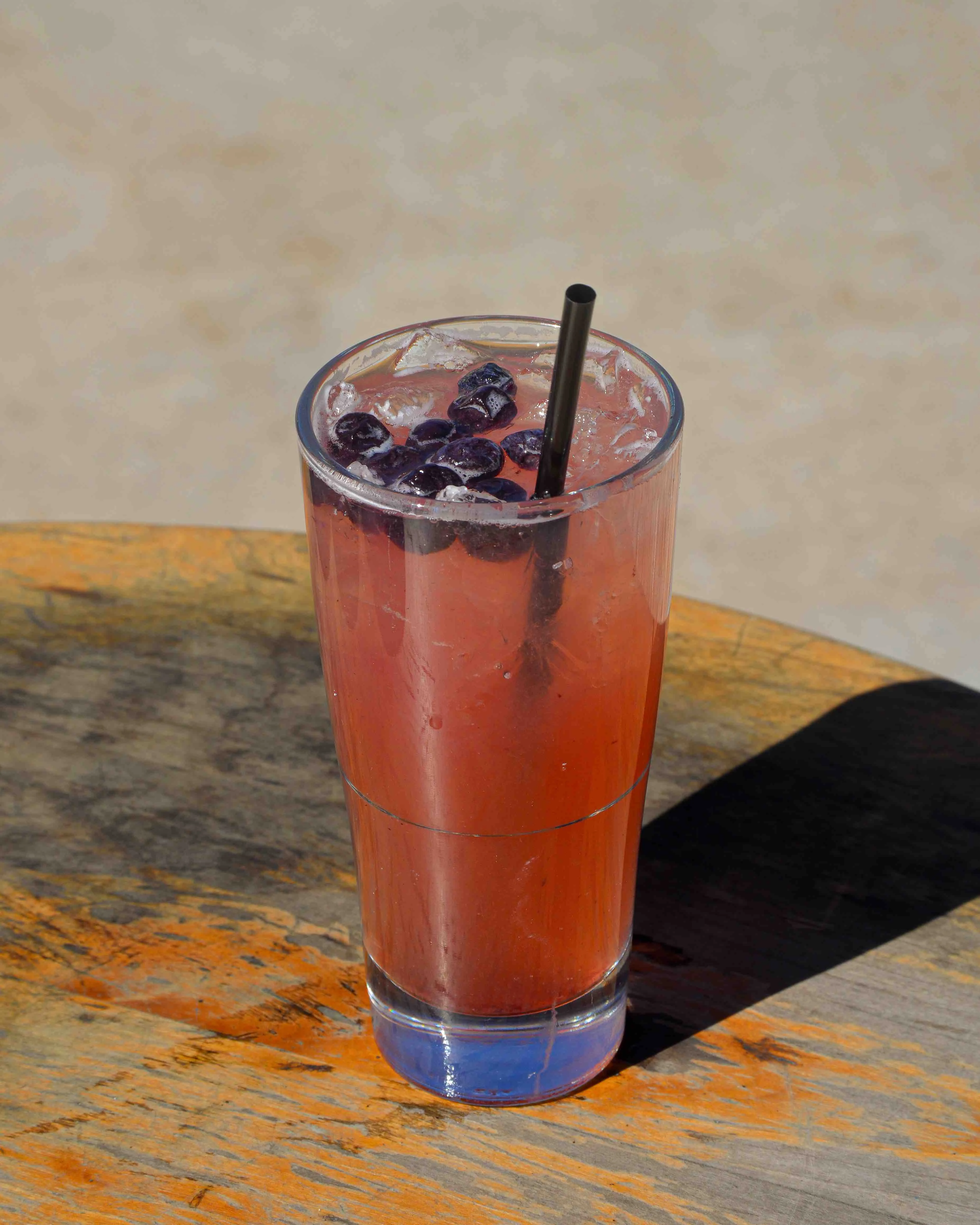 Bourbon Blueberry Spritz cocktail on a wooden table outside in the sun