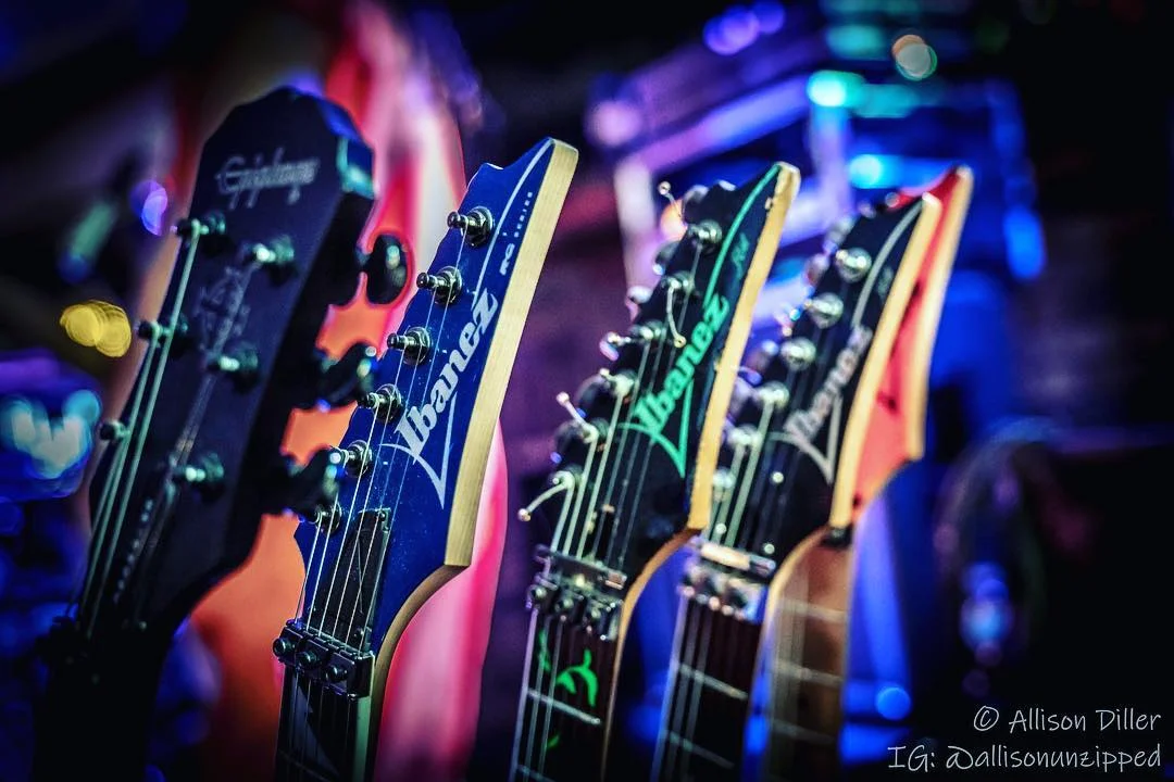 A close-up of multiple electric guitar heads, showcasing the brand and design details under dim lighting.