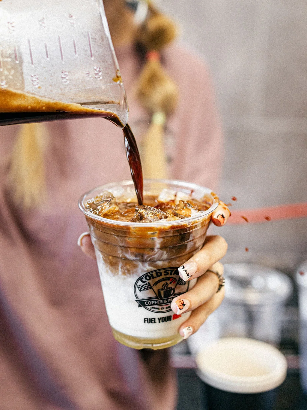 A person adding brown sugar to a cup of coffee while seated at a table.