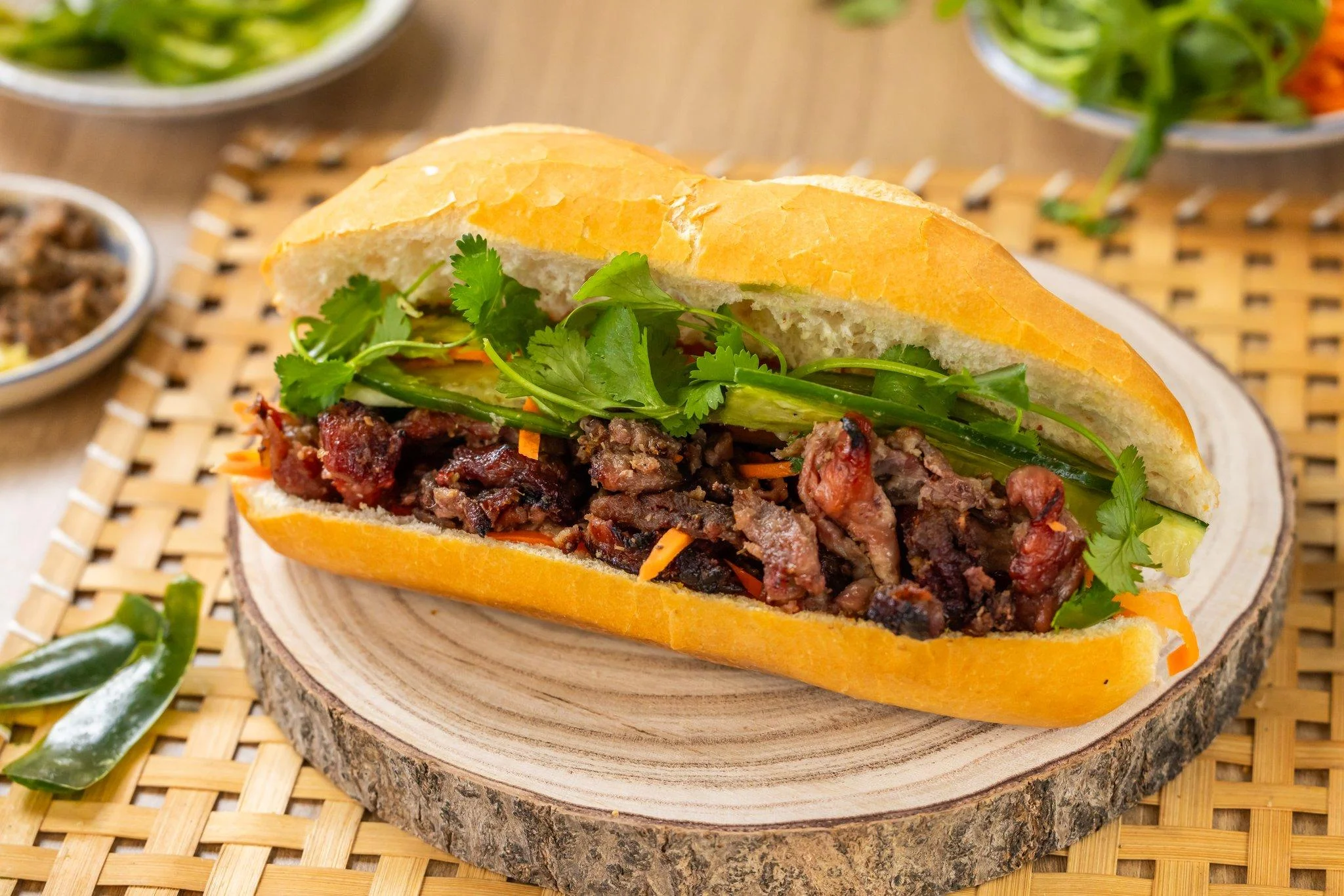 A close-up of a Vietnamese burger featuring grilled meat, fresh greens, and crispy carrots in a baguette.