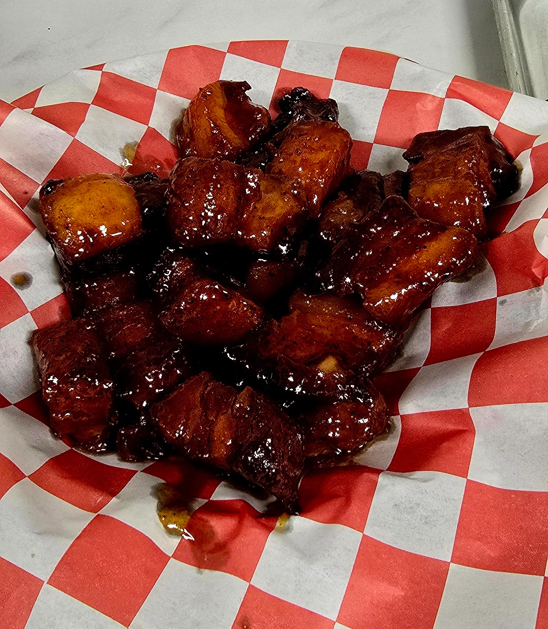 A plate of glazed, caramelized pork belly pieces on a checkered paper.