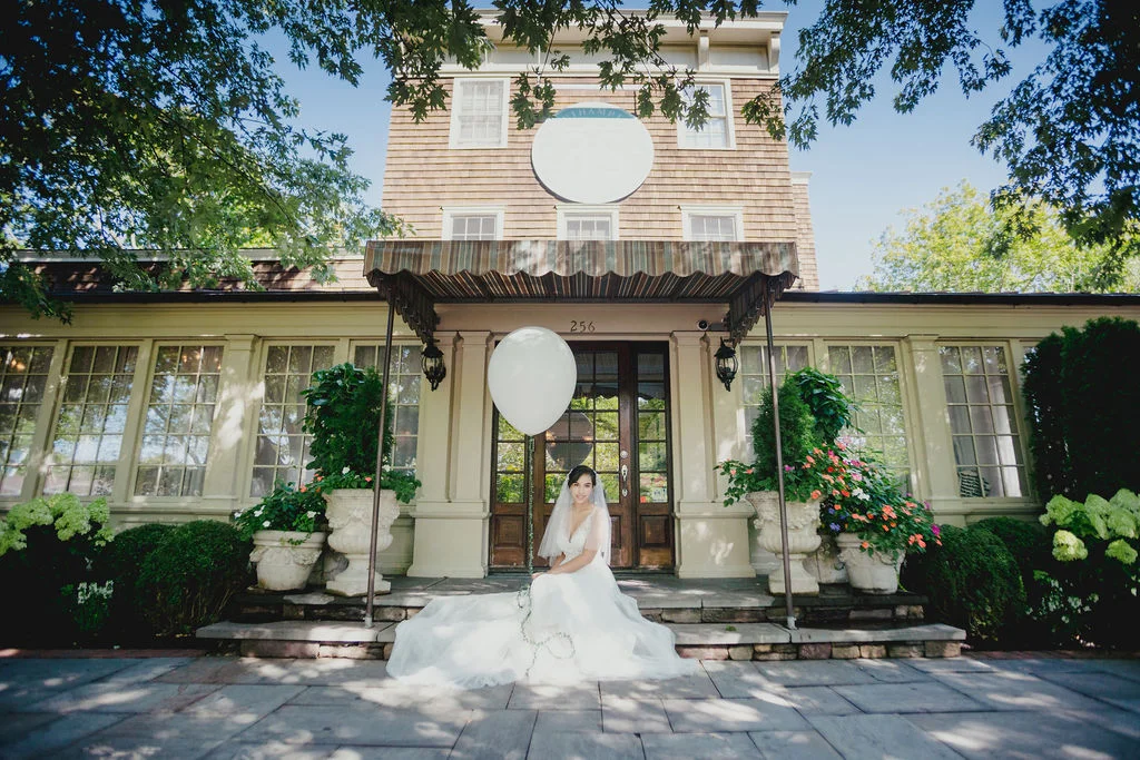 Bride sitting on steps of a charming venue with a balloon