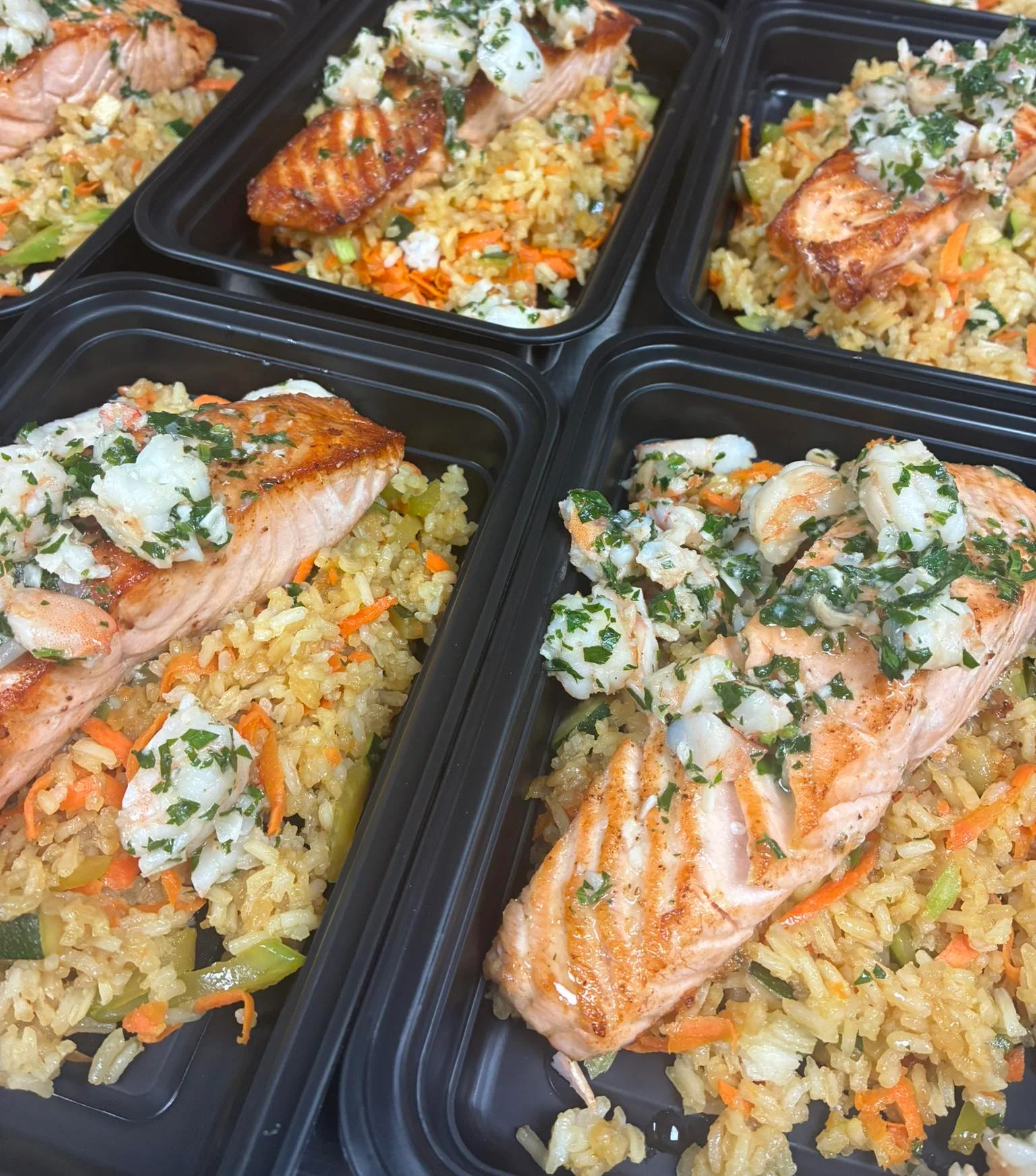 Grilled salmon with rice and vegetables in meal prep containers.