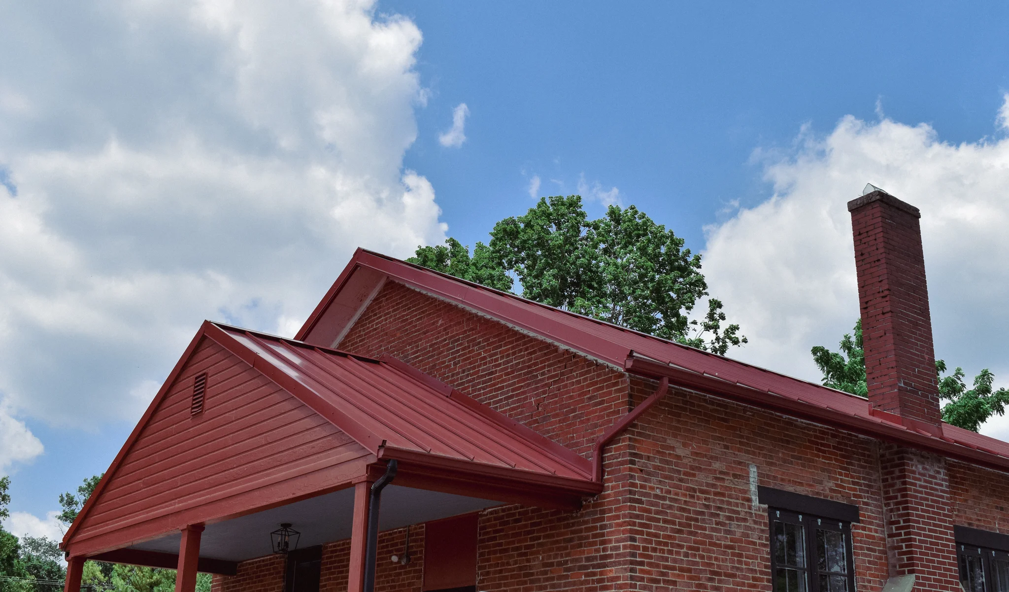 Red brick house with a metal roof under a blue sky