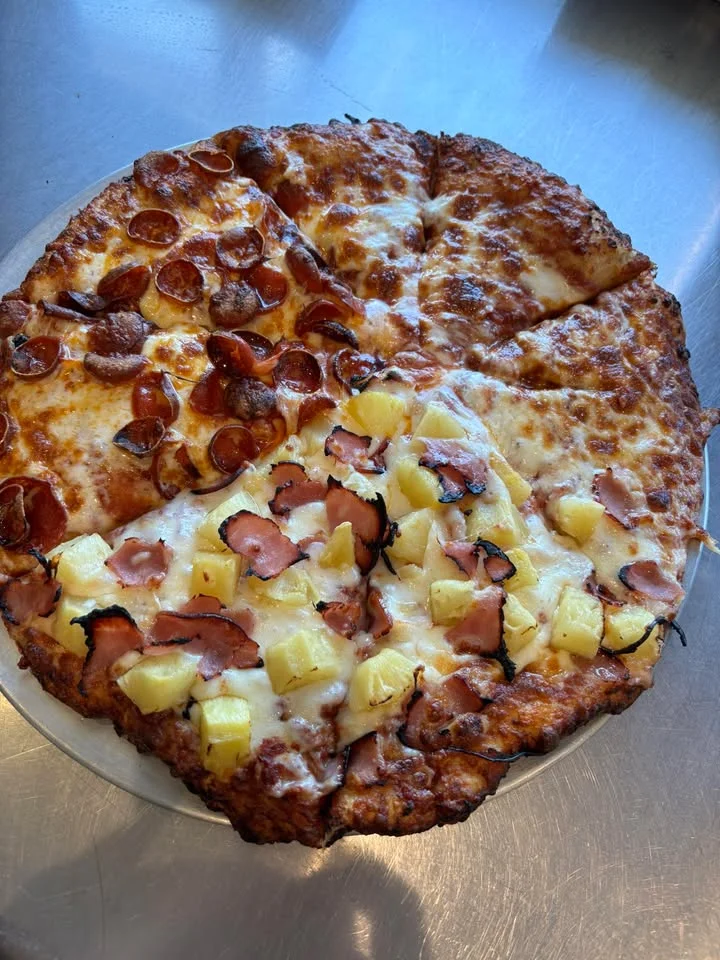 A large pizza divided into four sections, with toppings including pepperoni, ham, and pineapple.