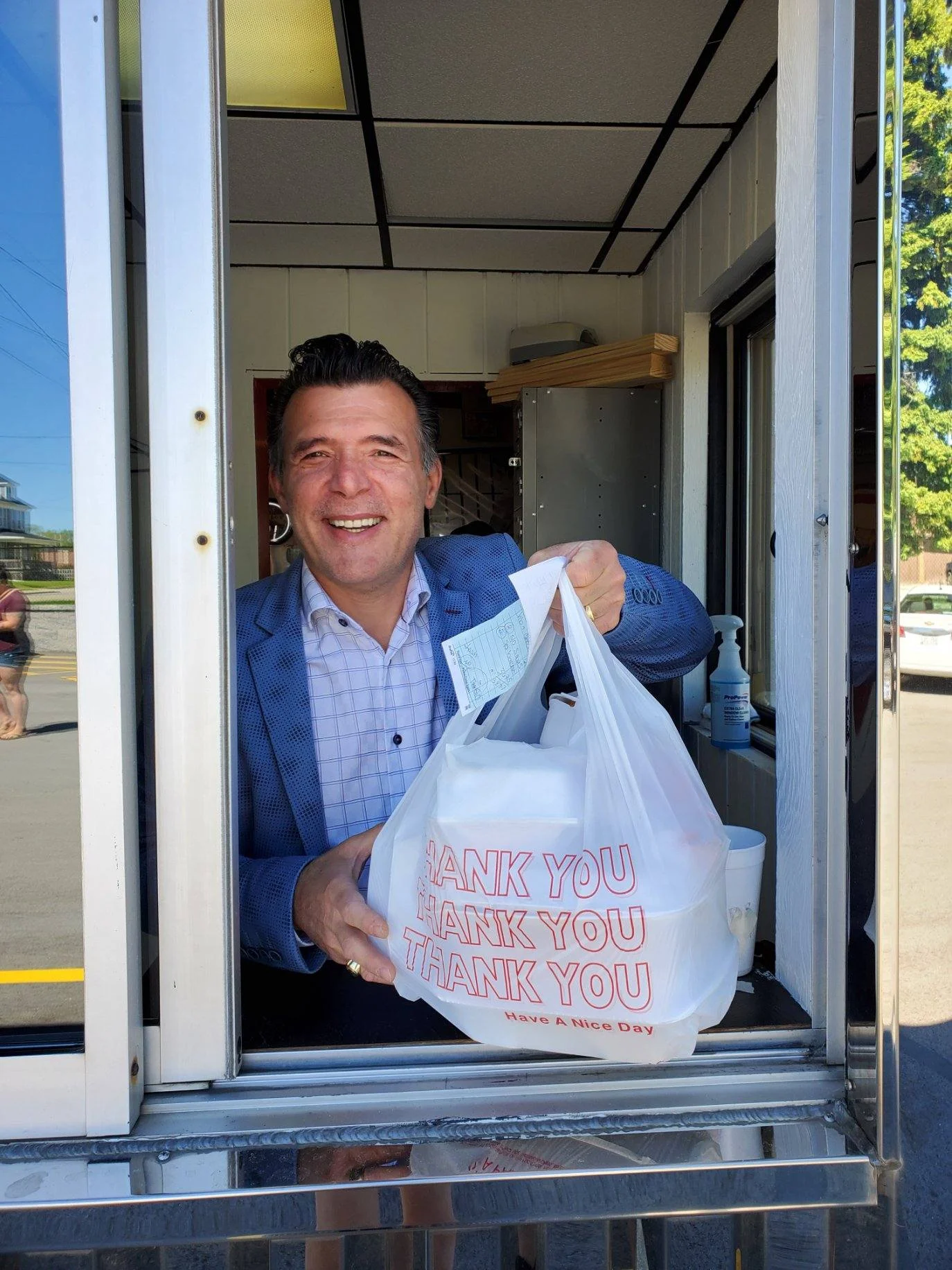 Smiling man at a restaurant window handing out takeout bag