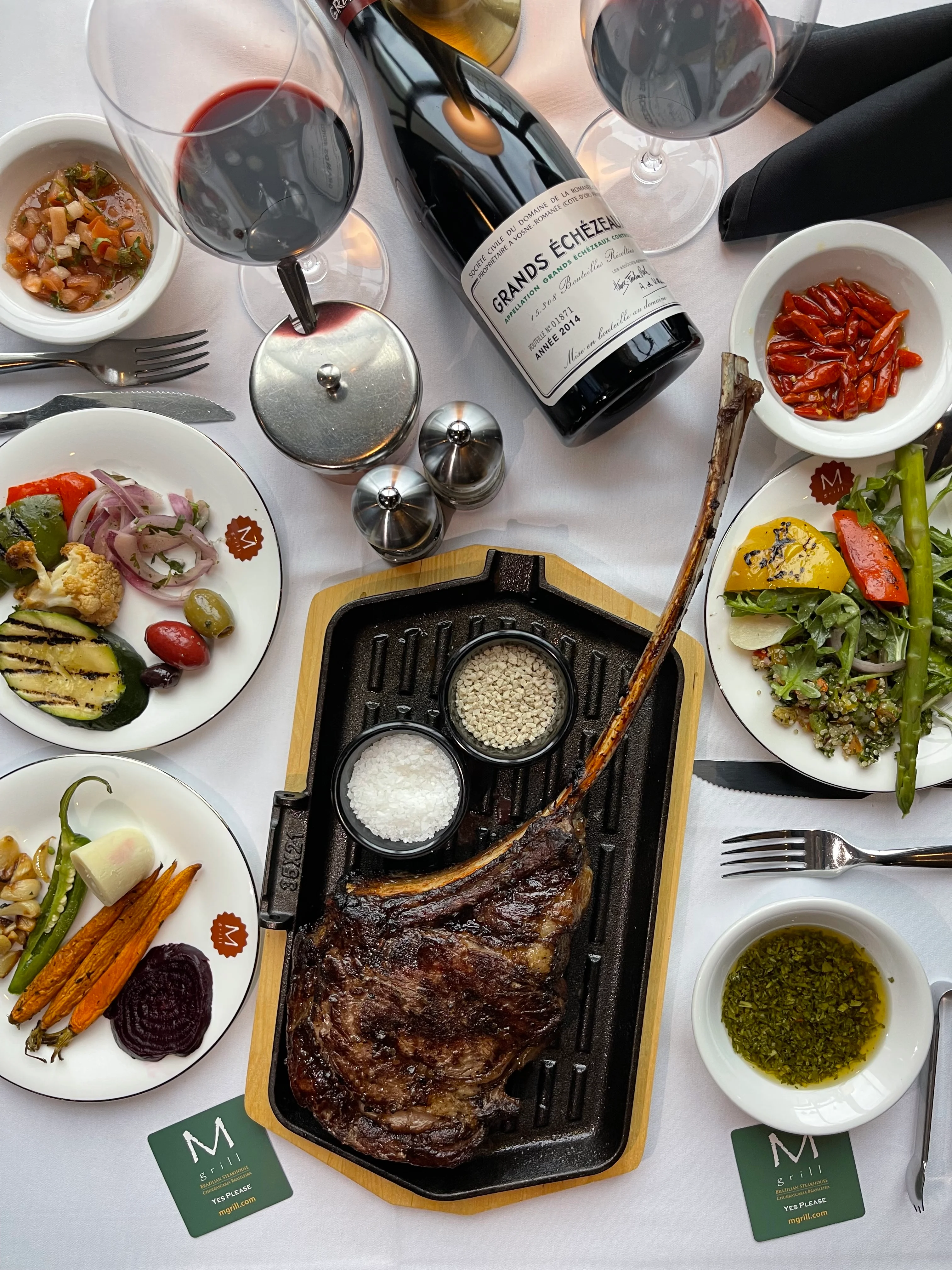 Grilled tomahawk steak served with sides and red wine