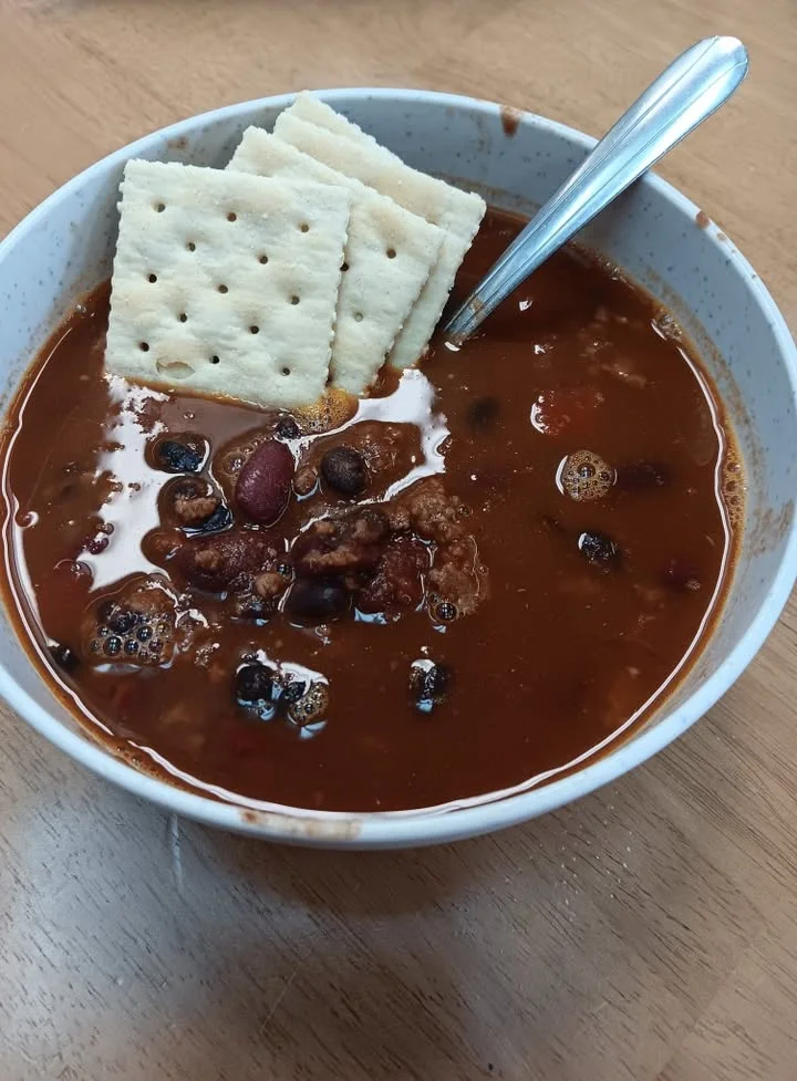 A bowl of chili topped with crackers. The chili is rich in color with visible beans, and the crackers are placed neatly on top.