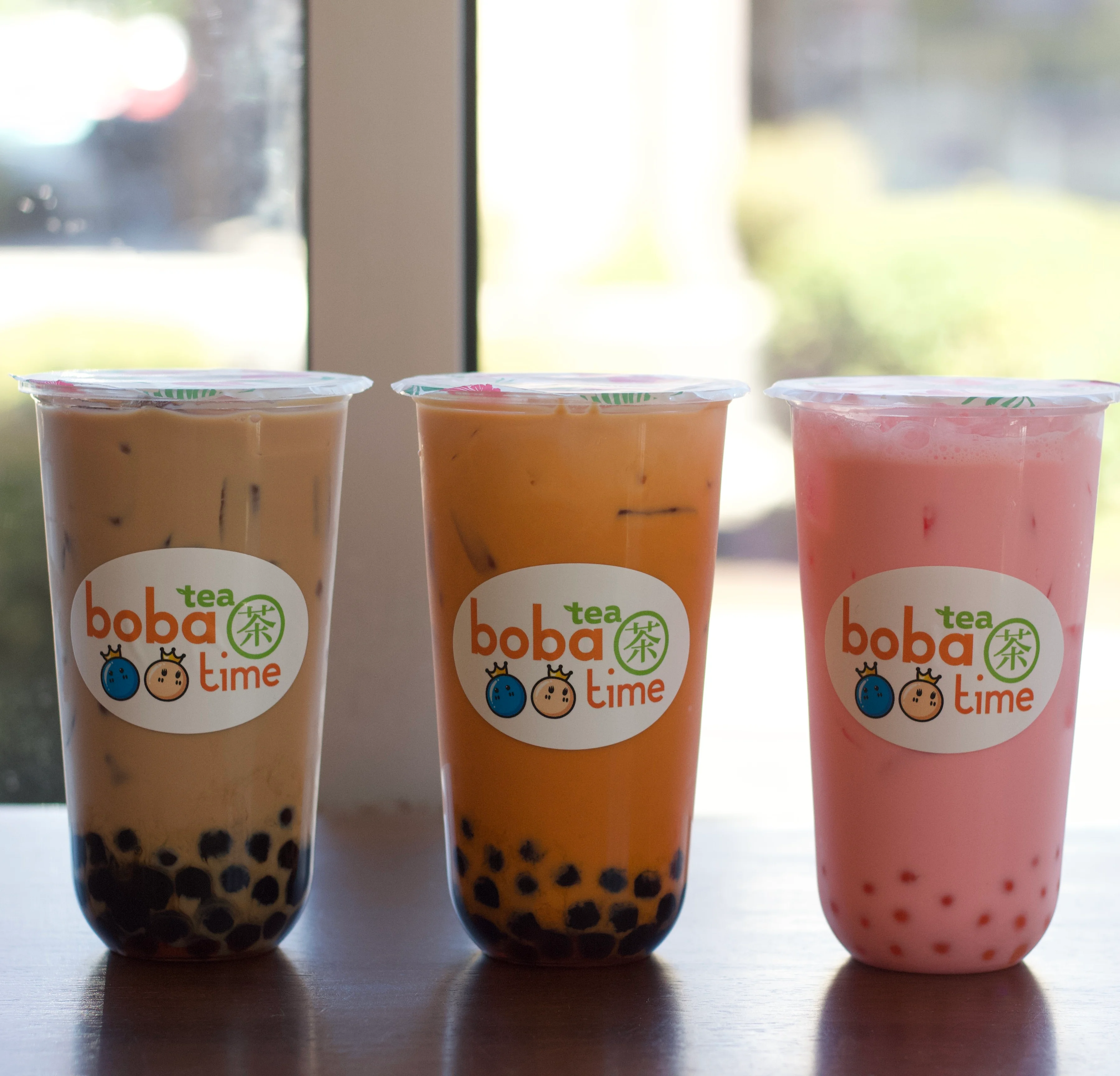 Colorful boba tea drinks in clear cups on a wooden table