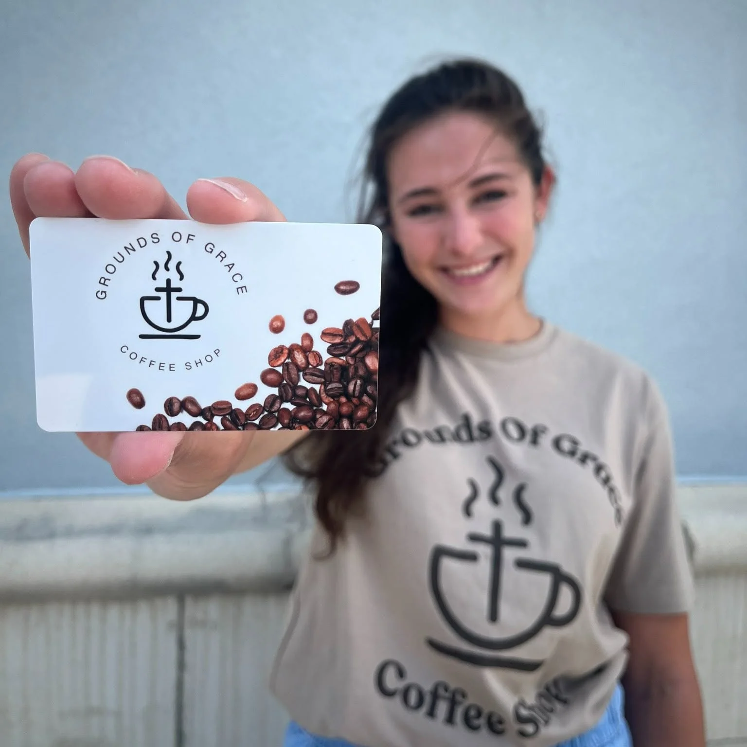 Smiling barista holding a coffee shop loyalty card outside Grounds of Grace