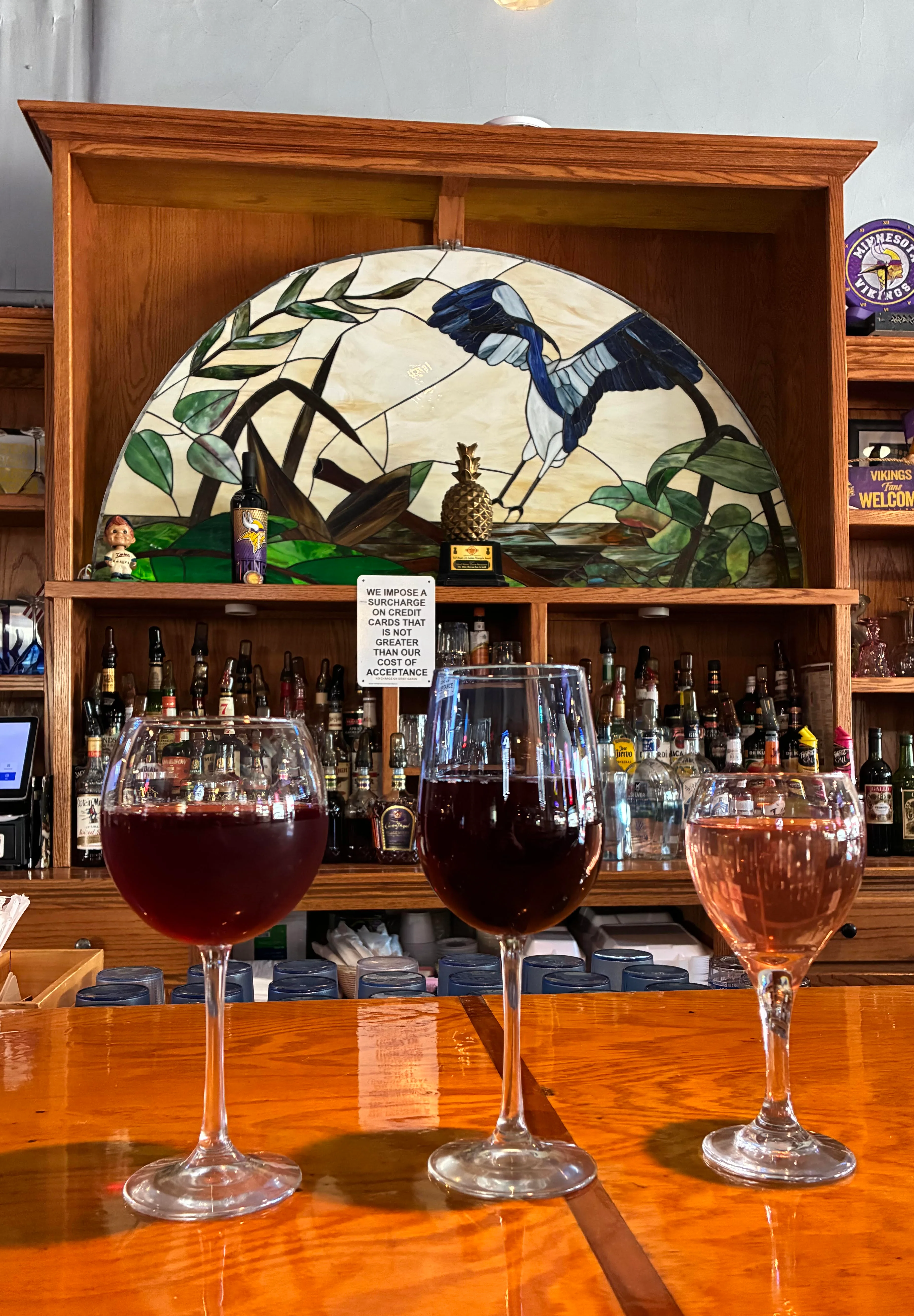 Three glasses of wine on a bar with a stained glass backdrop.
