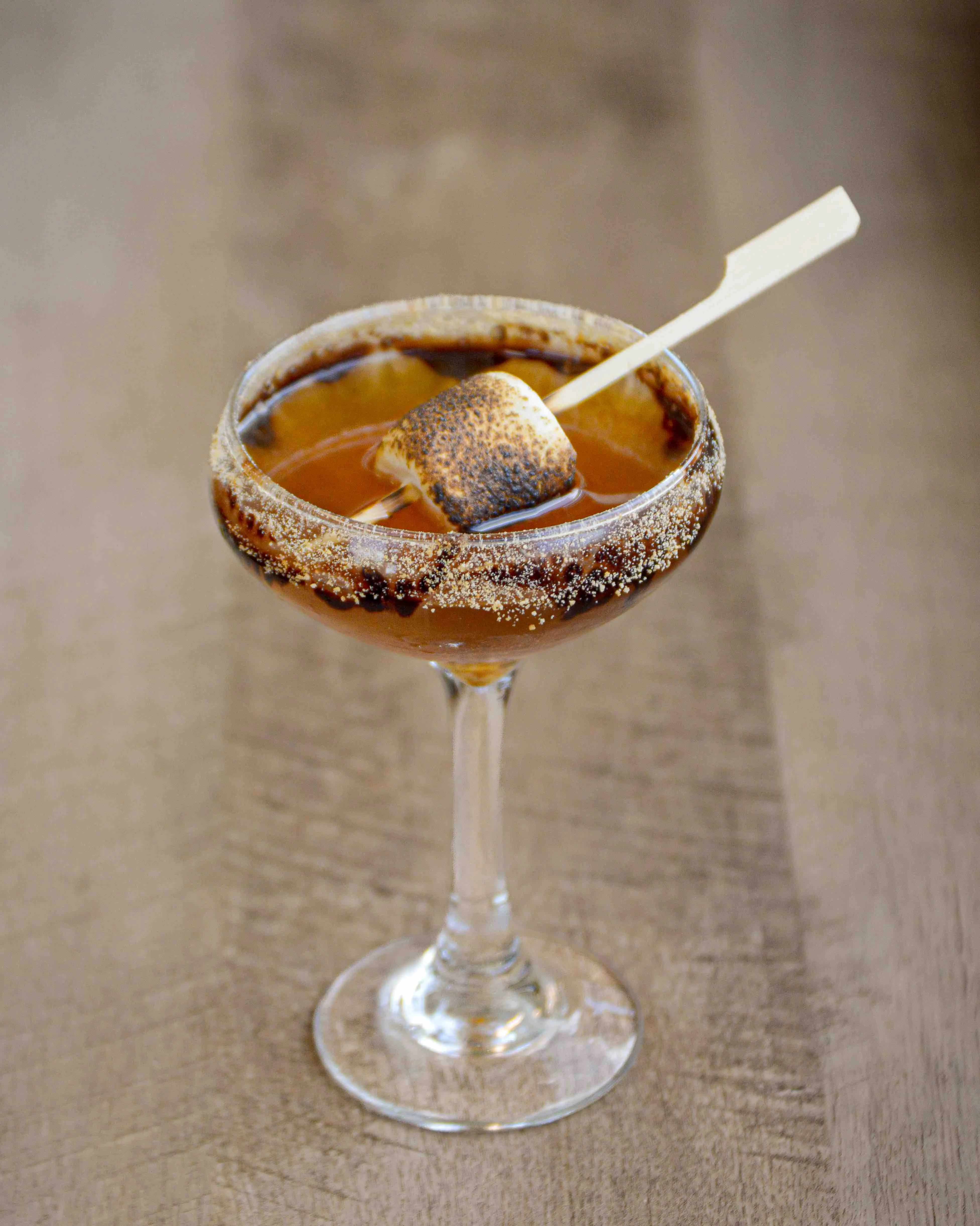 Smoked S'more Manhattan on a wooden table with a roasted marshmallow