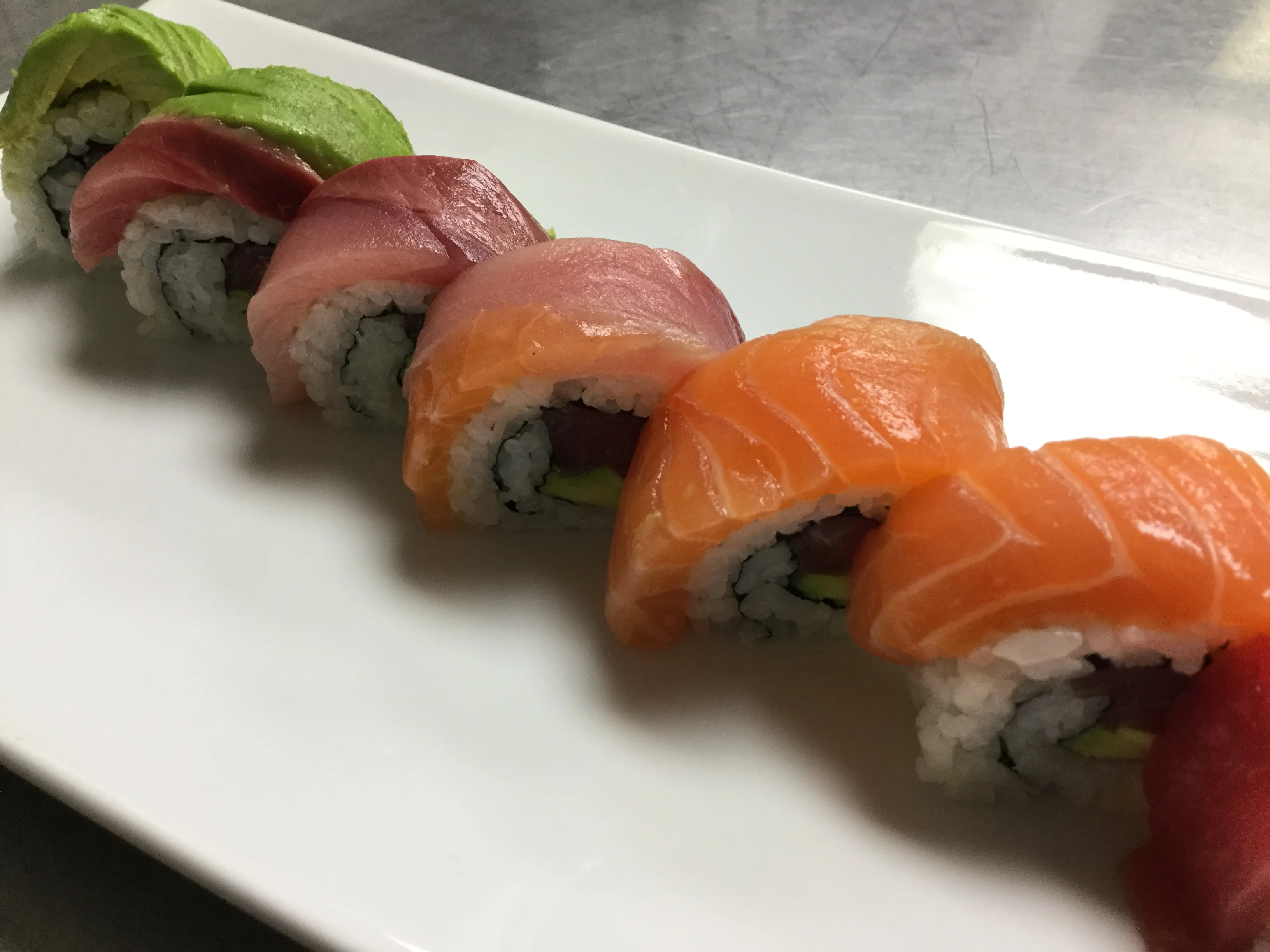 A plate of sushi rolls featuring rice, fish, and black sesame seeds. The rolls are neatly arranged on a white plate.