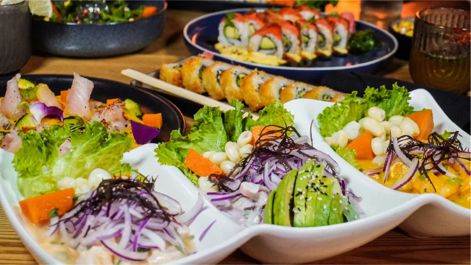 A variety of colorful sushi and fresh salads on a wooden table.