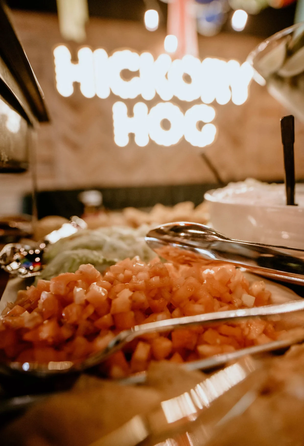 A close-up of a platter with diced tomatoes and other toppings, in the background is a neon sign indicating a restaurant.