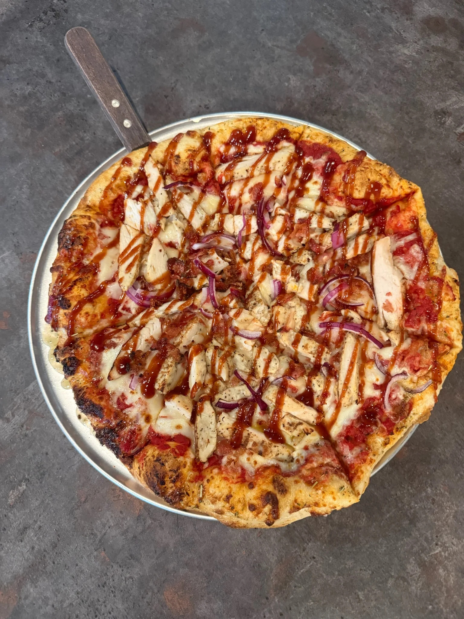 A delicious barbecue chicken pizza topped with red onions and drizzled with barbecue sauce.