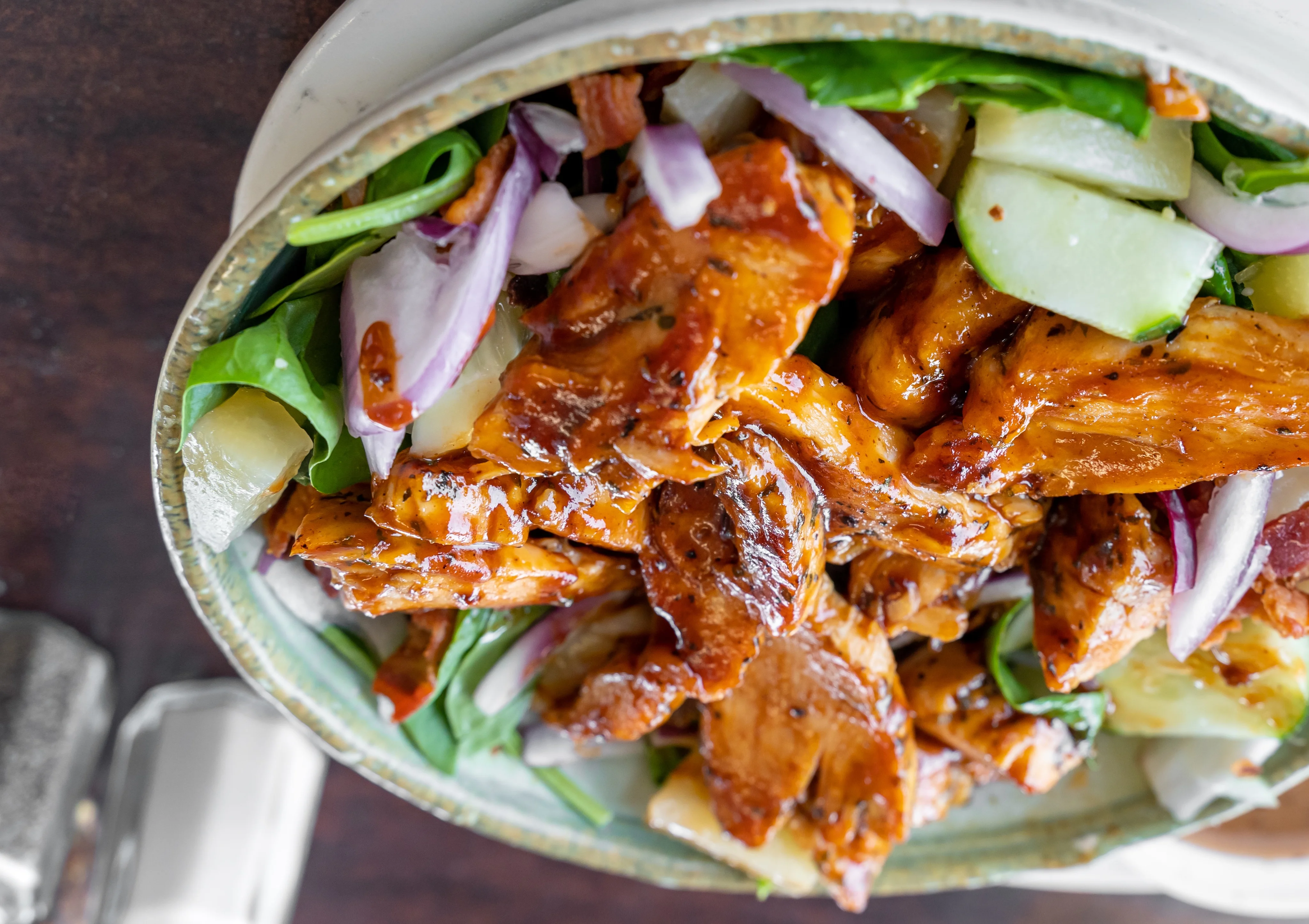 Bowl of a grilled chicken salad with glaze, served over lettuce and cucumber. 