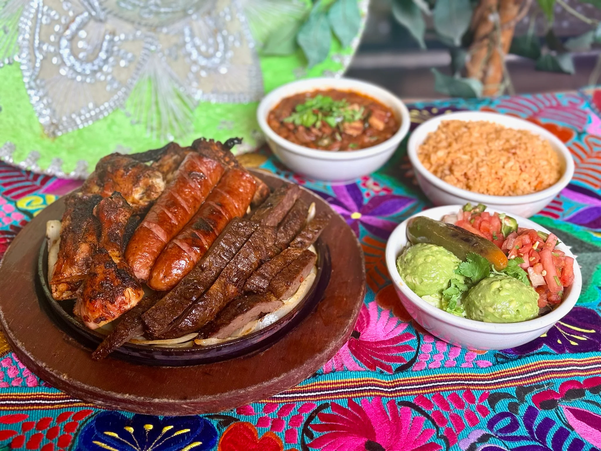 A sizzling platter of grilled meats with sides of rice, beans, and guacamole.