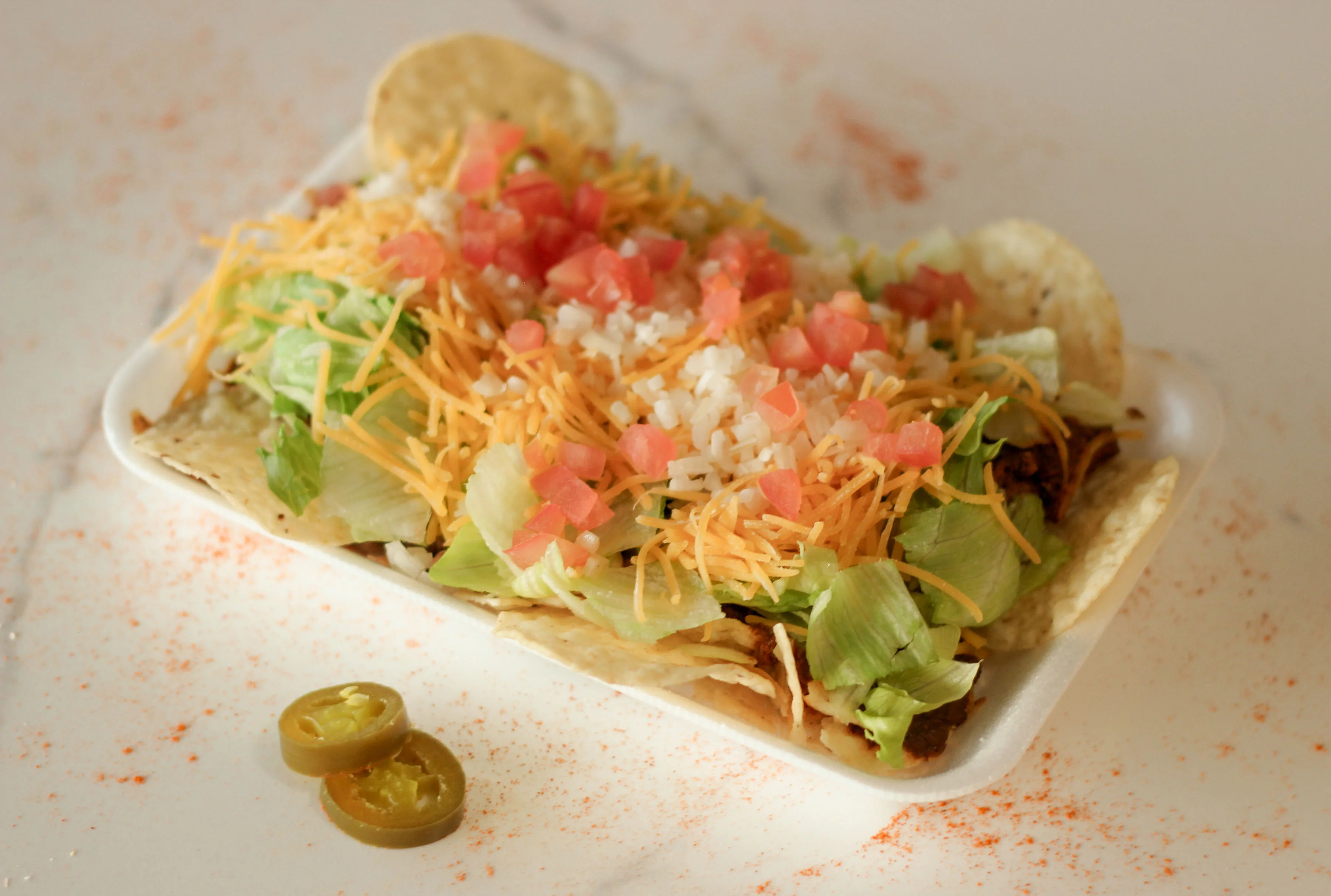A plate of tacos filled with shredded lettuce, diced tomatoes, cheese, and jalapeños, arranged beautifully.