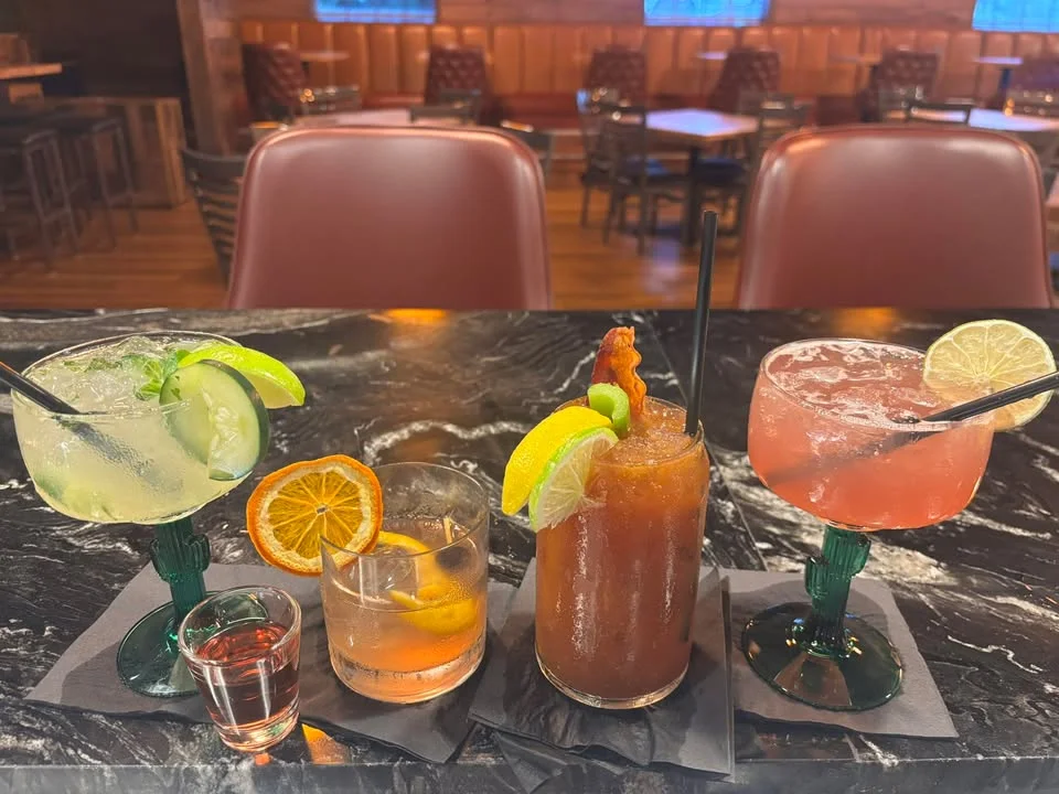 A collection of various cocktails displayed on a marble bar, featuring colorful garnishes like citrus slices and a shot glass.