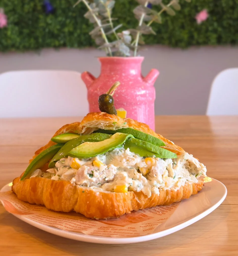 Croissant sandwich with chicken salad, avocado, and peppers in a vibrant café setting