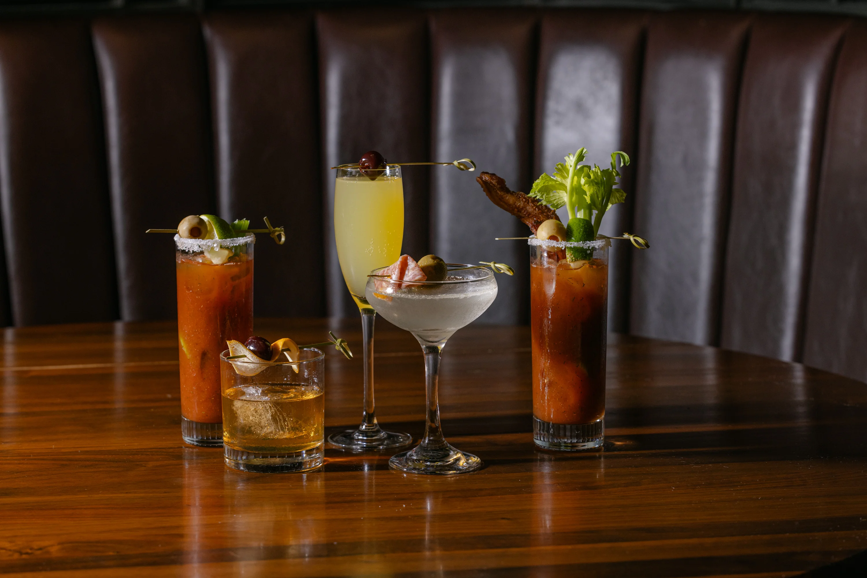 Four colorful cocktails on a wooden table in a restaurant setting.