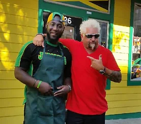 Two chefs posing outside a vibrant Jamaican restaurant