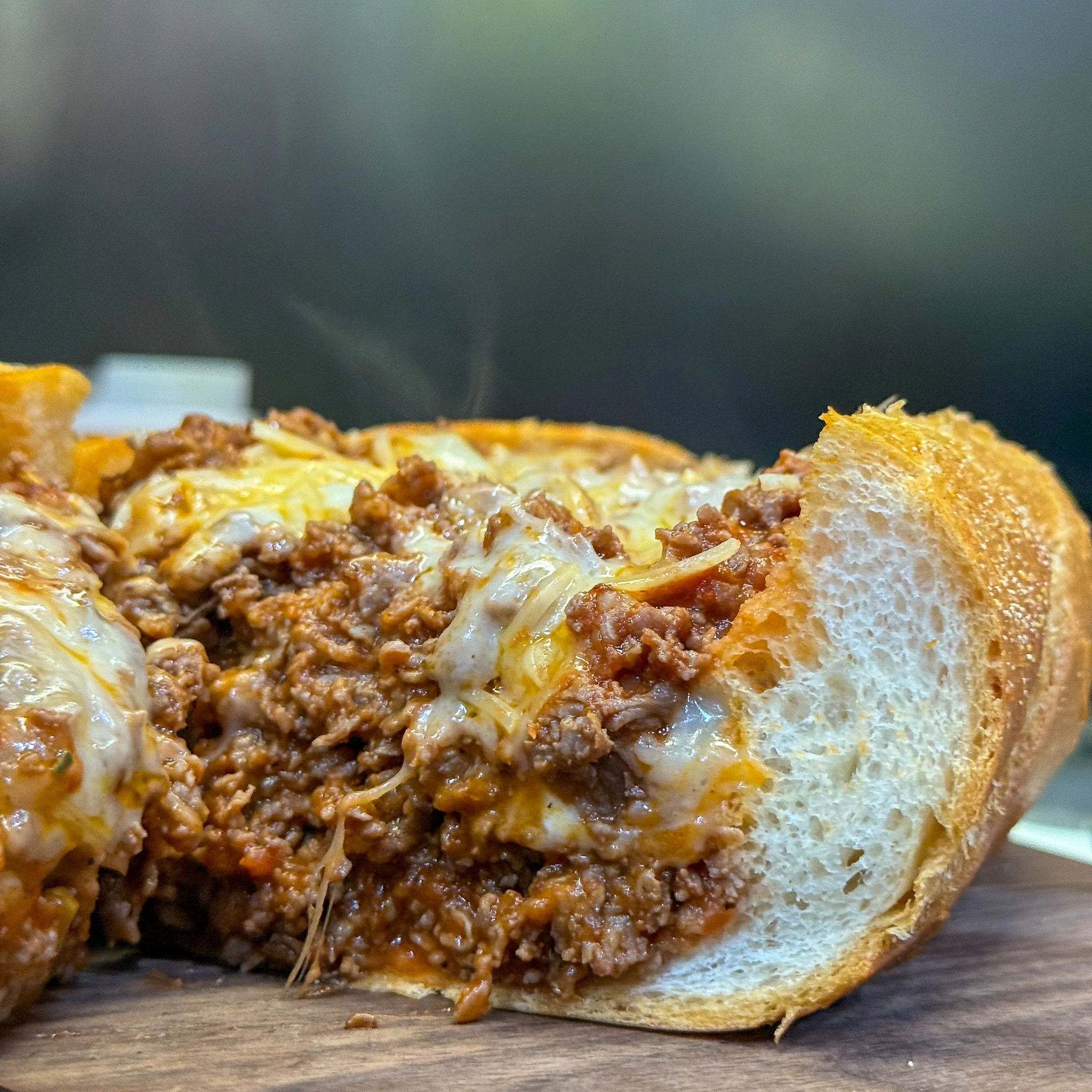 Close-up of a pizza steak hoagie filled with seasoned beef, marinara sauce, and melted cheese inside a fresh toasted roll