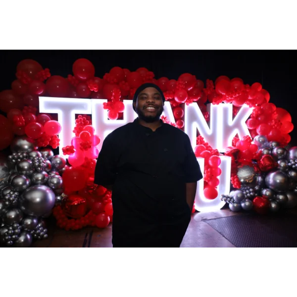 Chef posing in front of a festive 'Thank You' balloon display