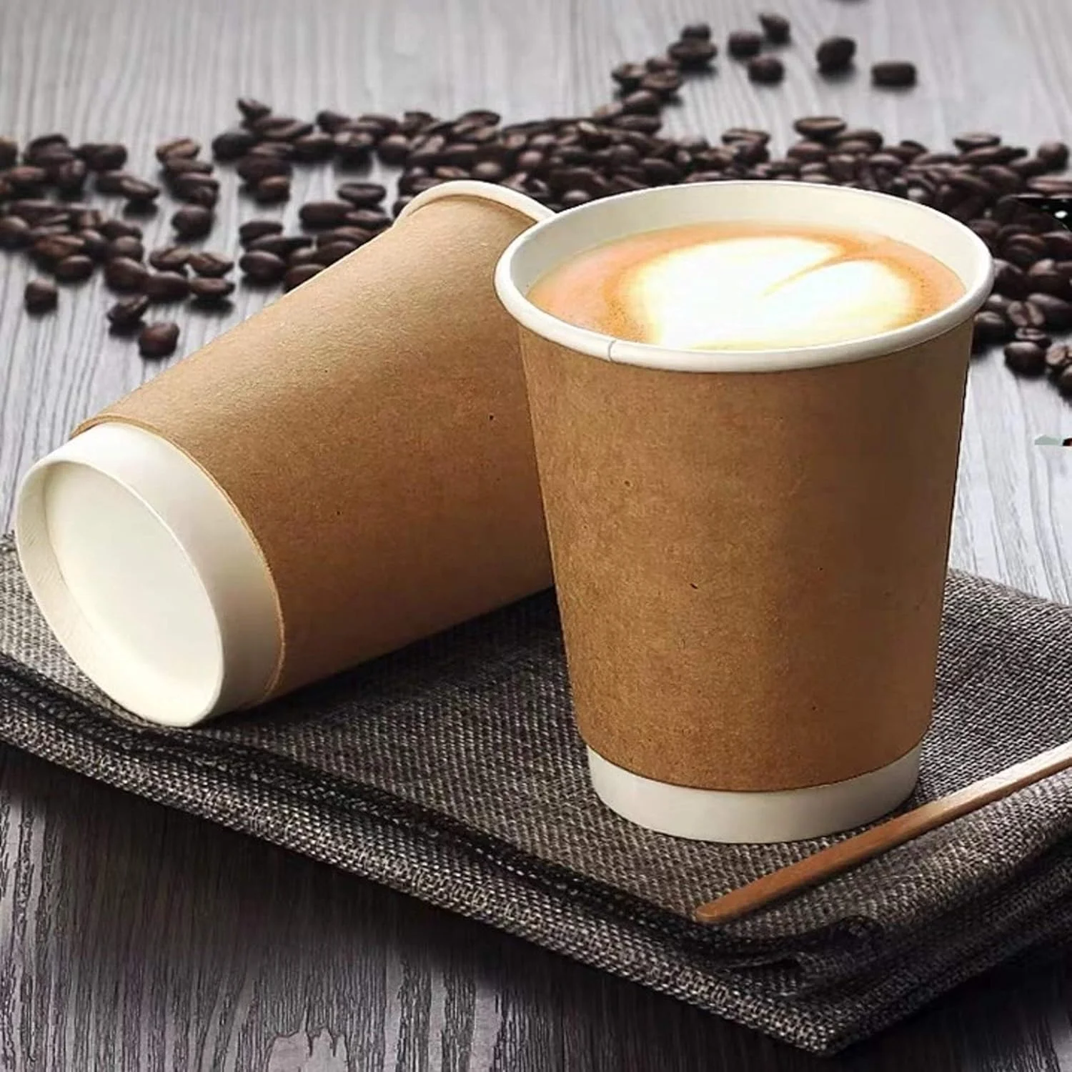Two coffee cups on a textured surface with coffee beans