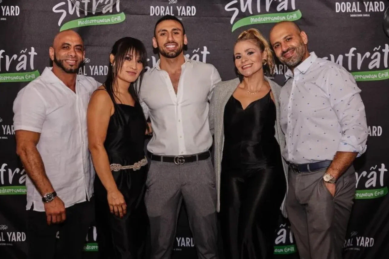 Three men wearing white shirts and gray pants stand alongside two women in black dresses. The men are the founders of Sufrat Mediterranean Grill.