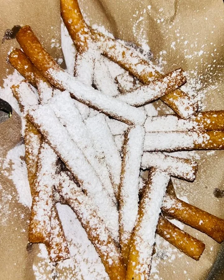 A serving of crispy fried dough sticks dusted with powdered sugar, arranged on brown paper.
