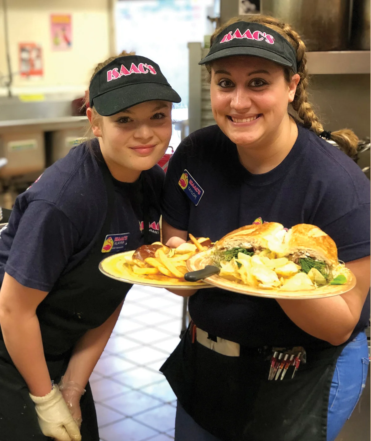 Two women in uniform proudly holding a tray filled with delicious food, ready to serve with smiles on their faces.