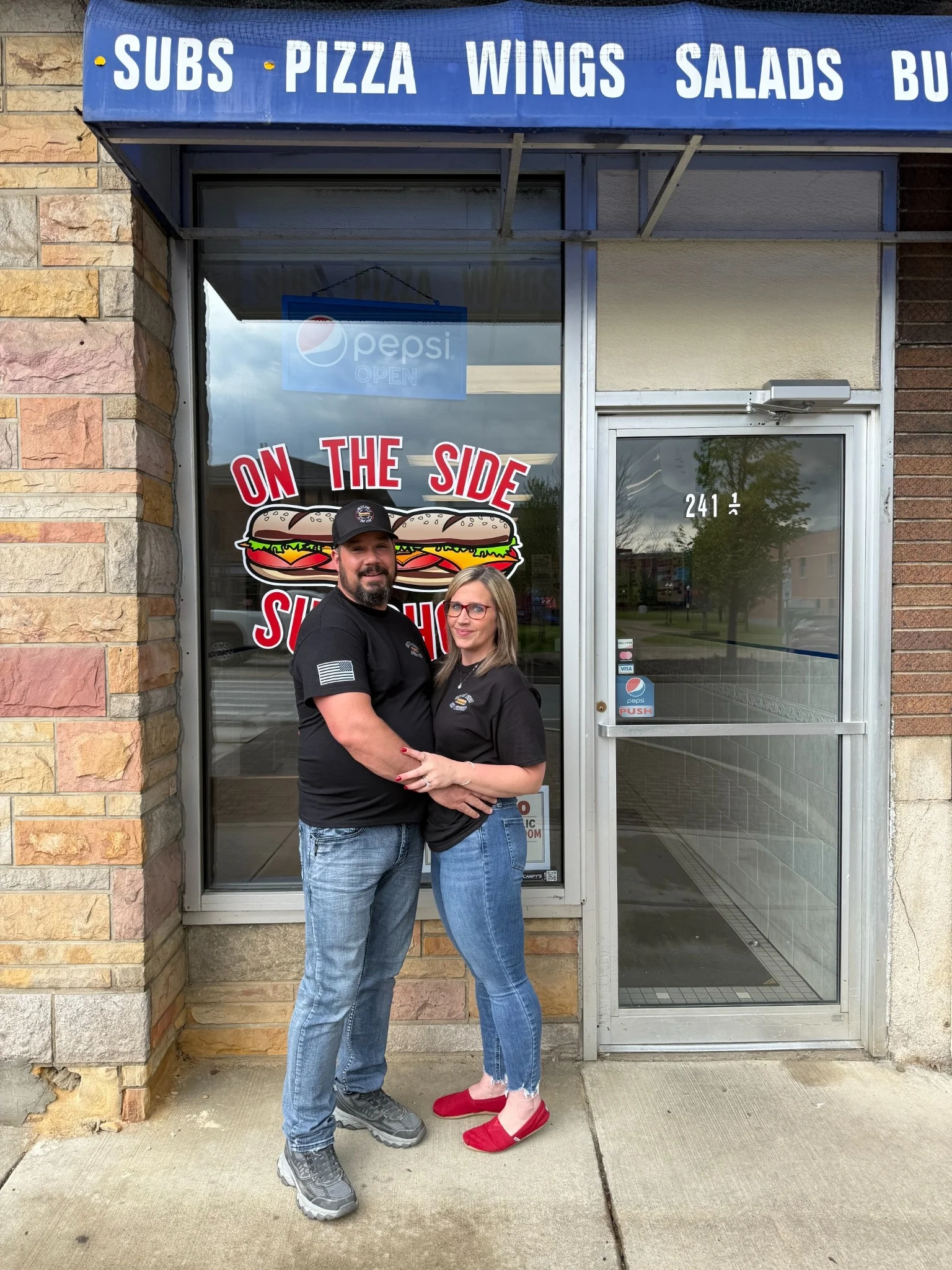 Couple in front of a sandwich shop with a welcoming sign