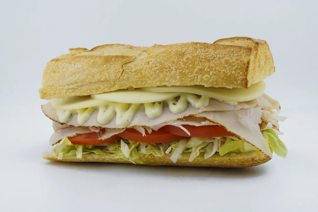 A sandwich layered with sliced turkey, lettuce, tomato, and mayonnaise in a crispy baguette.