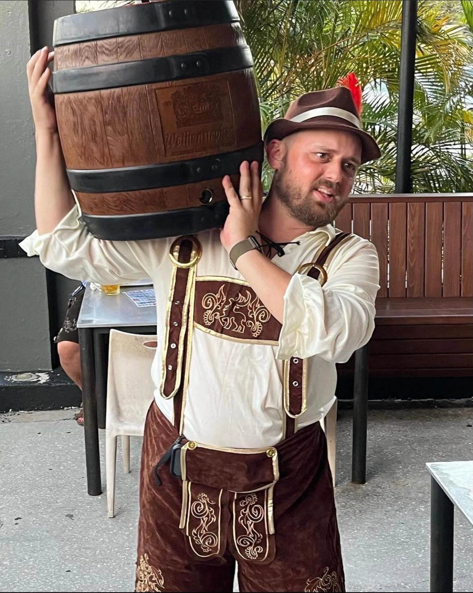 Man in traditional Bavarian attire holding a beer barrel at a festive event.