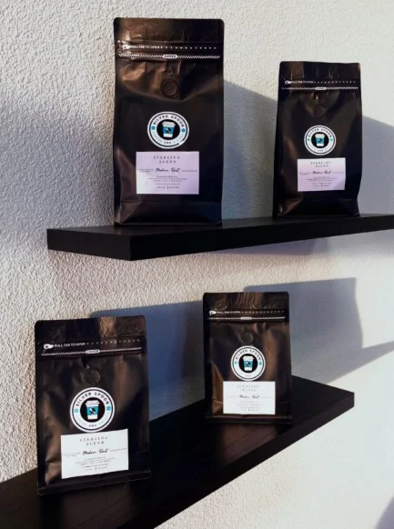 A collection of coffee bags displayed on a shelf. The bags are various sizes with a distinctive logo and label indicating the product.
