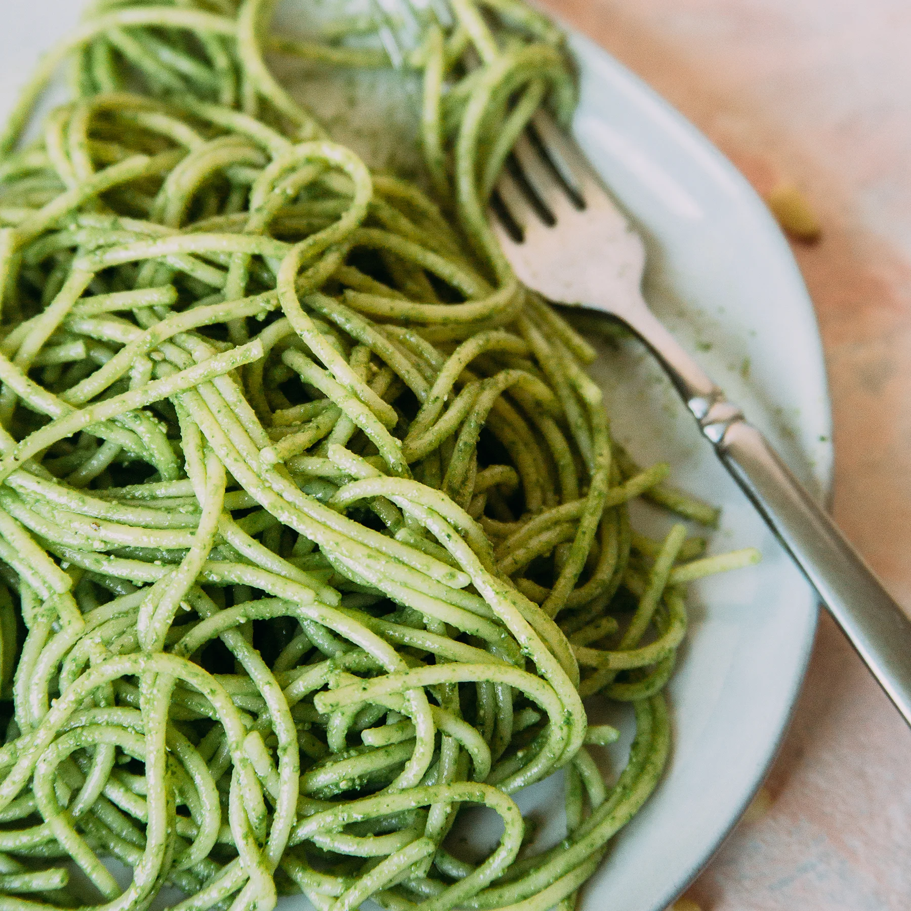 Plate of green spaghetti with a fork, showcasing a vibrant pesto dish.