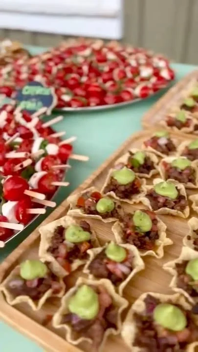 An assortment of small appetizers featuring bite-sized tortilla cups filled with seasoned meat and topped with green sauce, alongside skewers of cherry tomatoes and cheese.