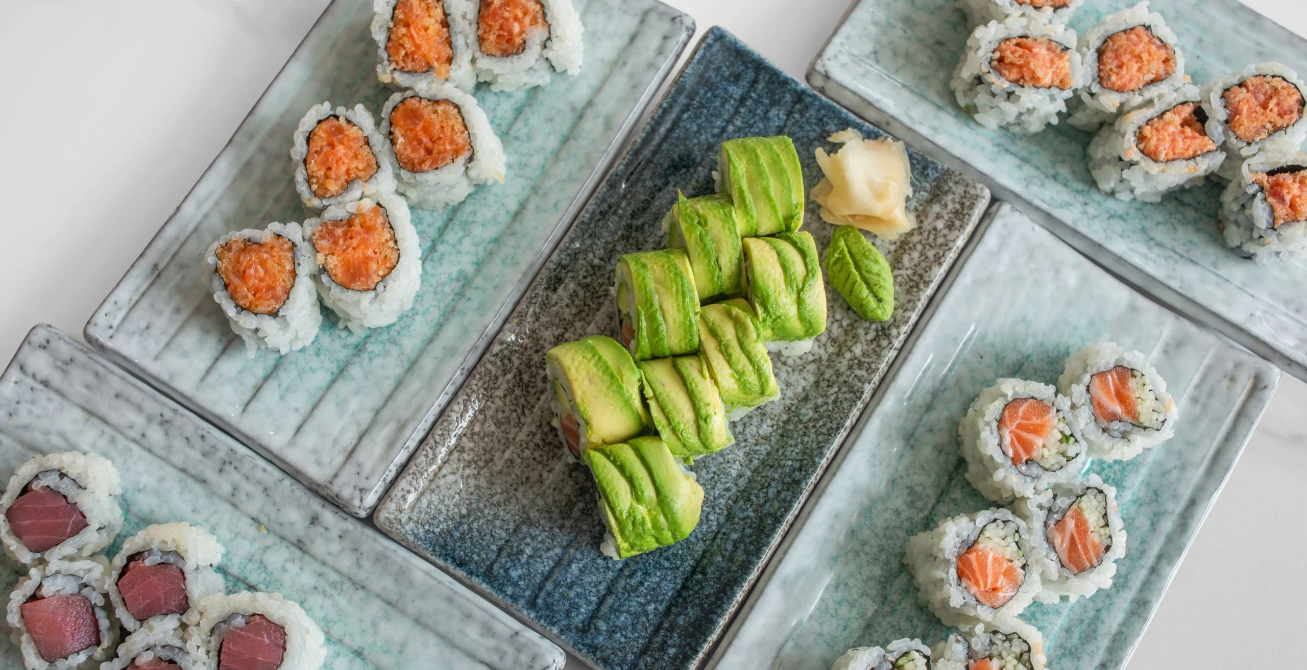 Assorted sushi rolls including salmon and avocado, presented on elegant plates