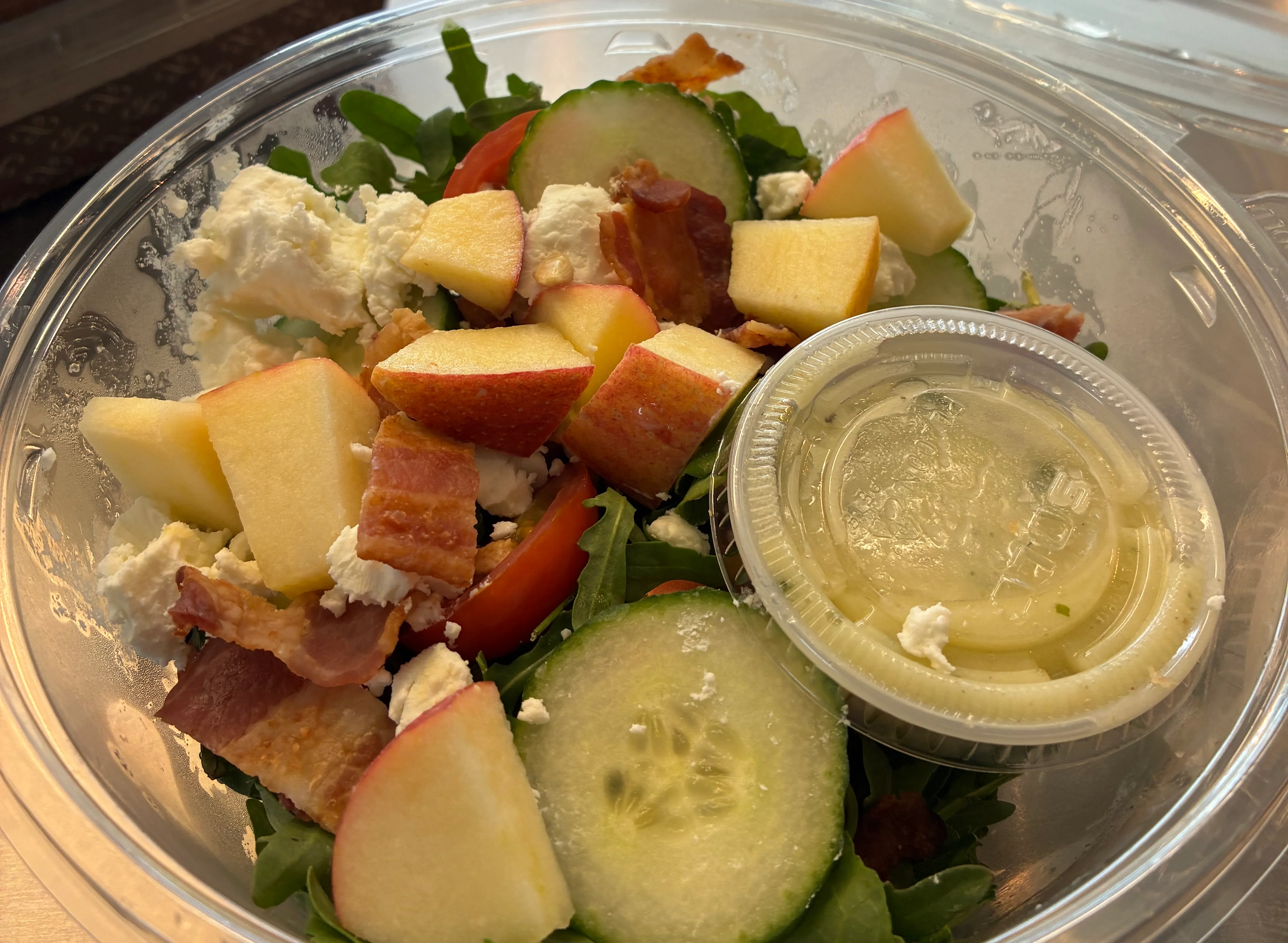 A rustic table setting featuring a vibrant salad bowl alongside two hearty sandwiches on a wooden cutting board. The salad includes greens, tomatoes, cucumbers, and croutons, while the sandwiches are filled with assorted meats and vegetables.