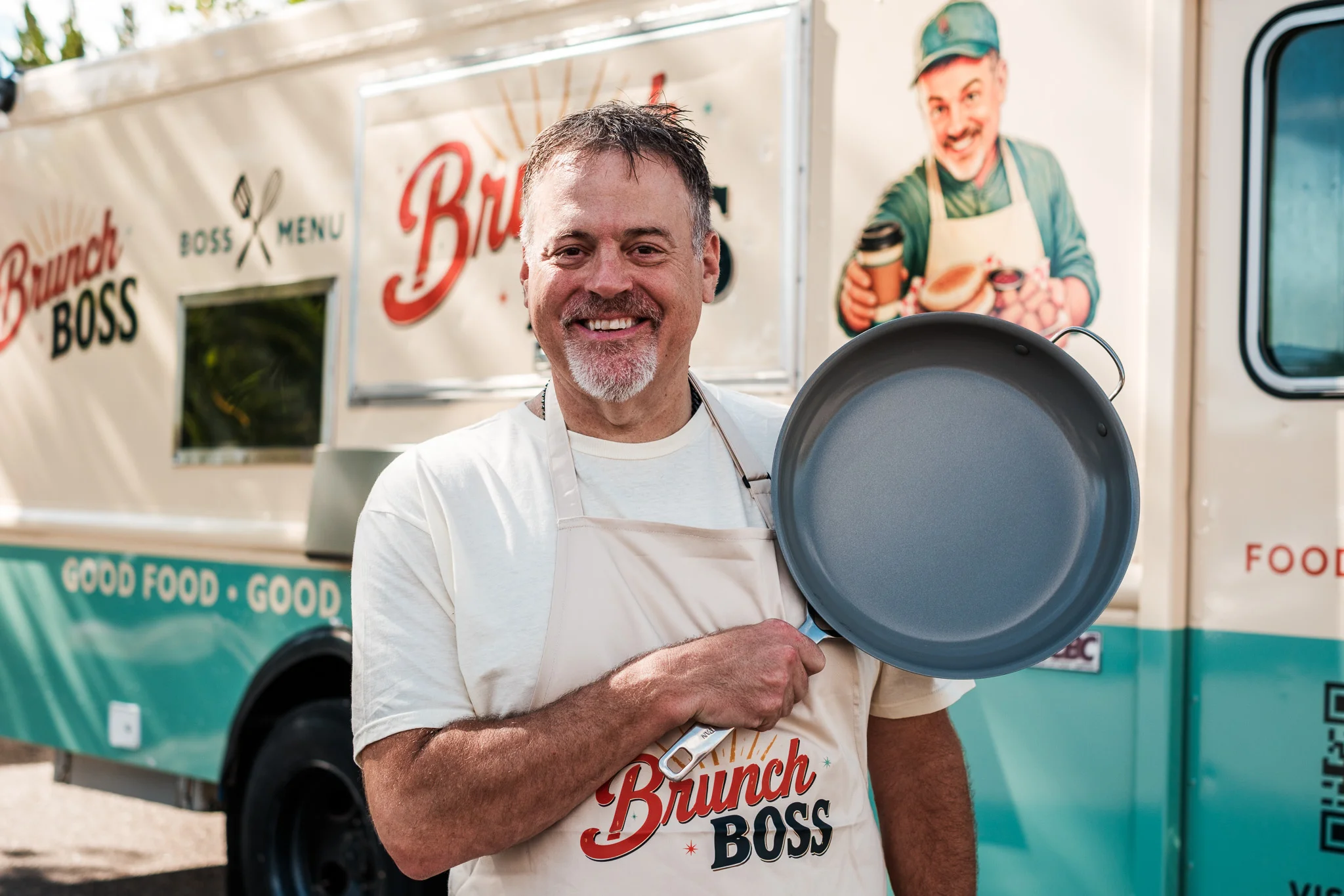 Chef holding a frying pan in front of a food truck