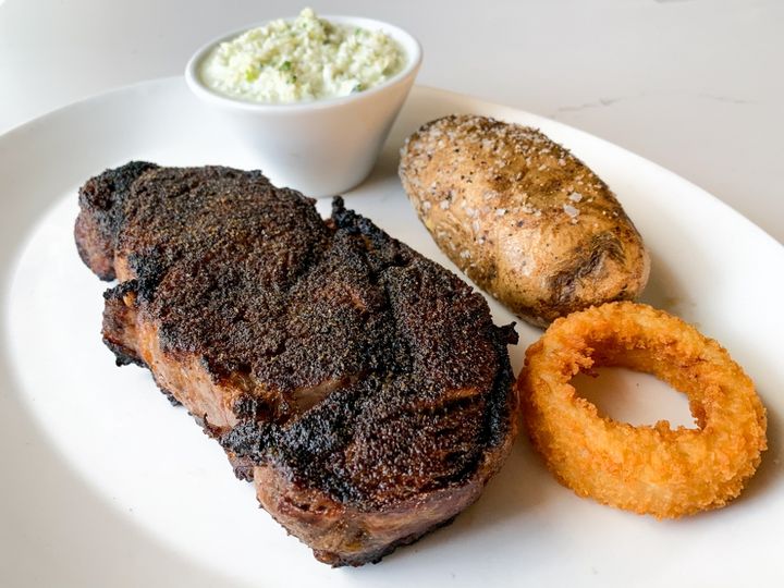 Steak with a baked potato, onion ring, and coleslaw
