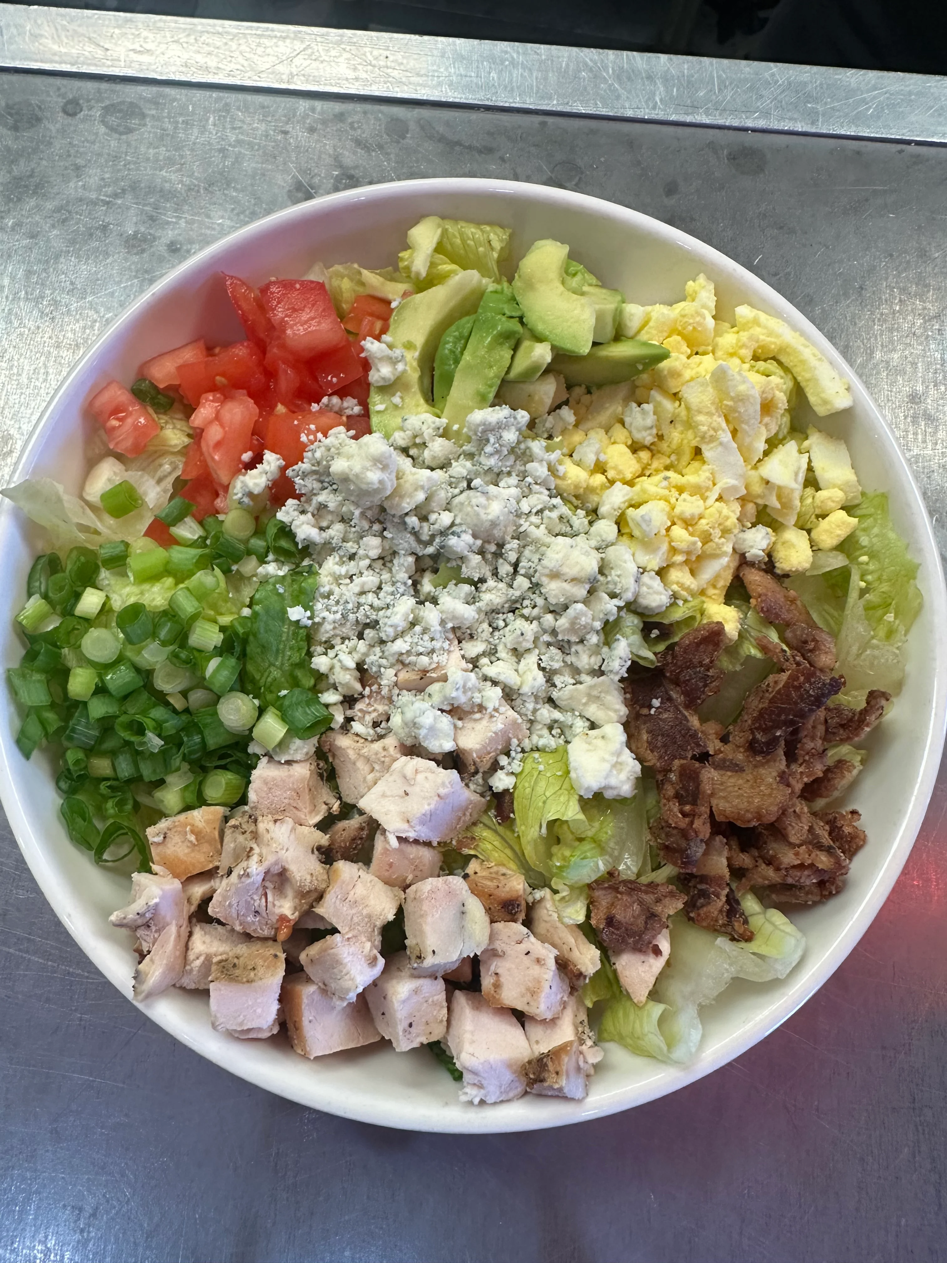 A colorful salad bowl featuring diced chicken, chopped vegetables, and various toppings arranged neatly.