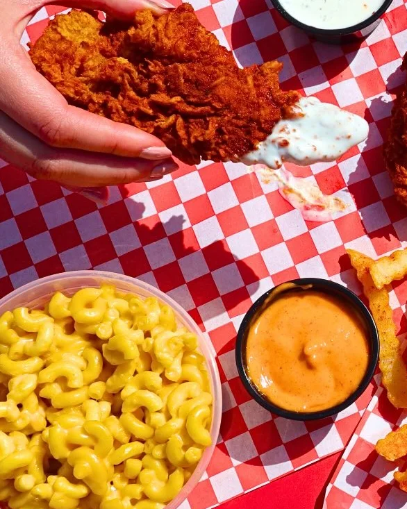 A serving of crispy fried chicken strips arranged in a tray with pickles and a small cup of dipping sauce.