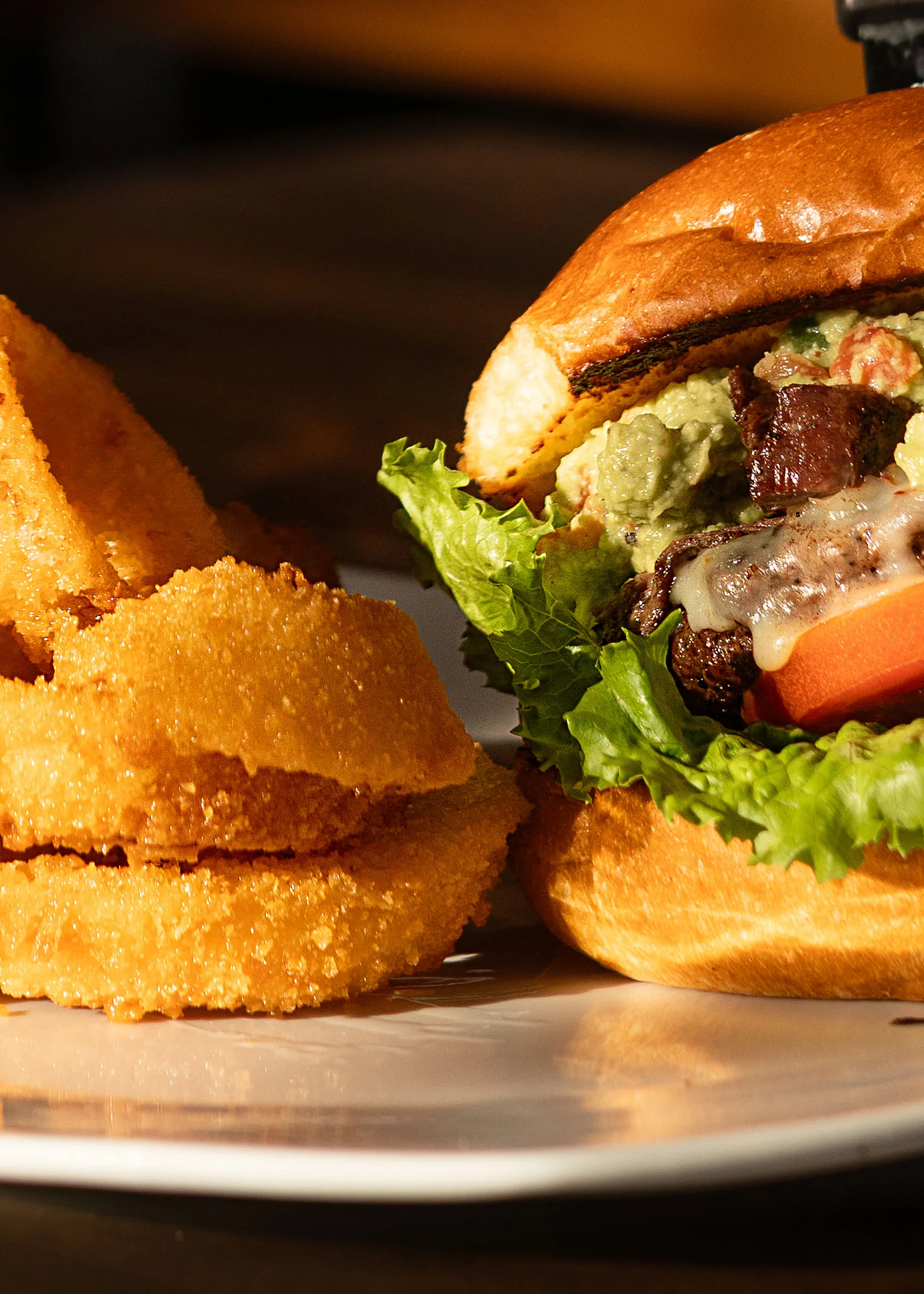 A close-up of a gourmet burger next to crispy onion rings, featuring fresh ingredients and vibrant colors.