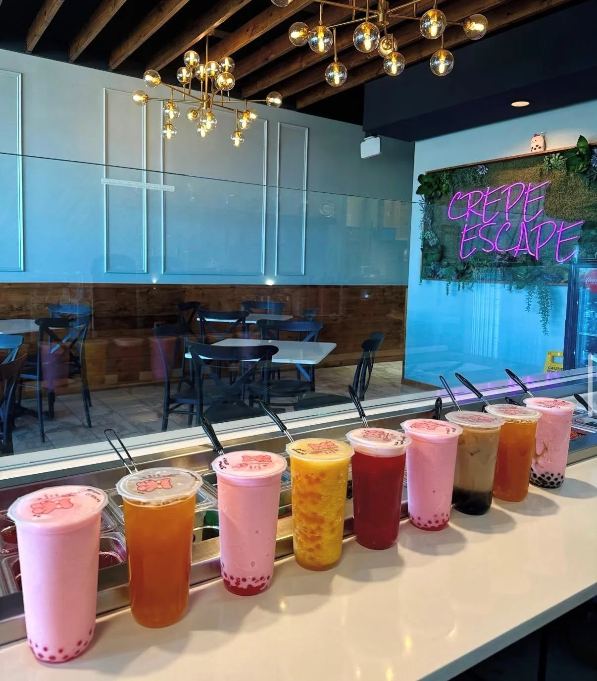 A colorful display of various beverages lined up on a counter in a modern cafe, with a stylish sign in the background.