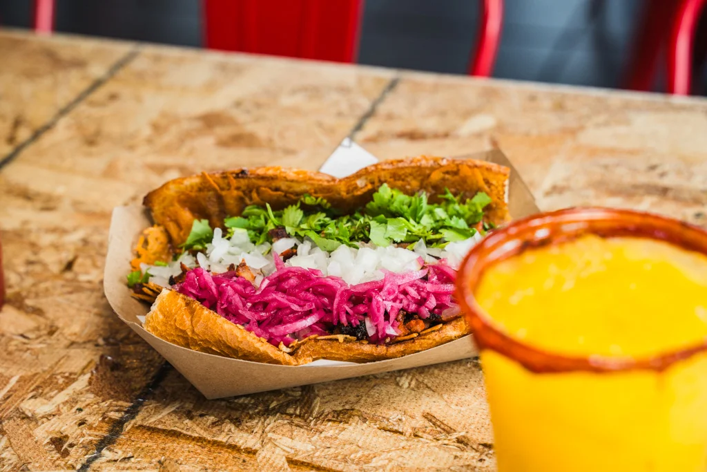 Three tacos with toppings and a lime wedge on a wooden table.