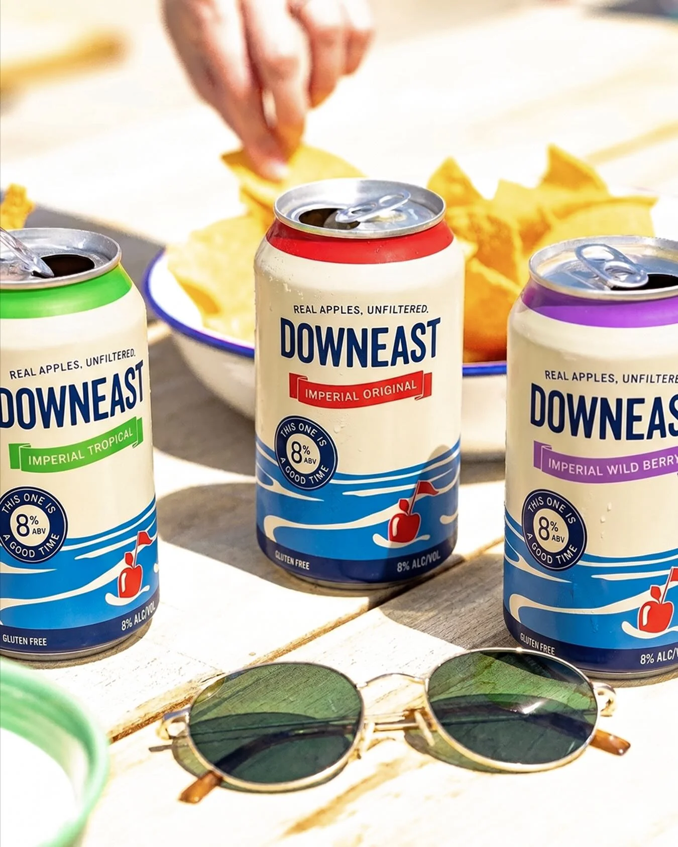 Three cans of Downeast cider with tortilla chips on a wooden table