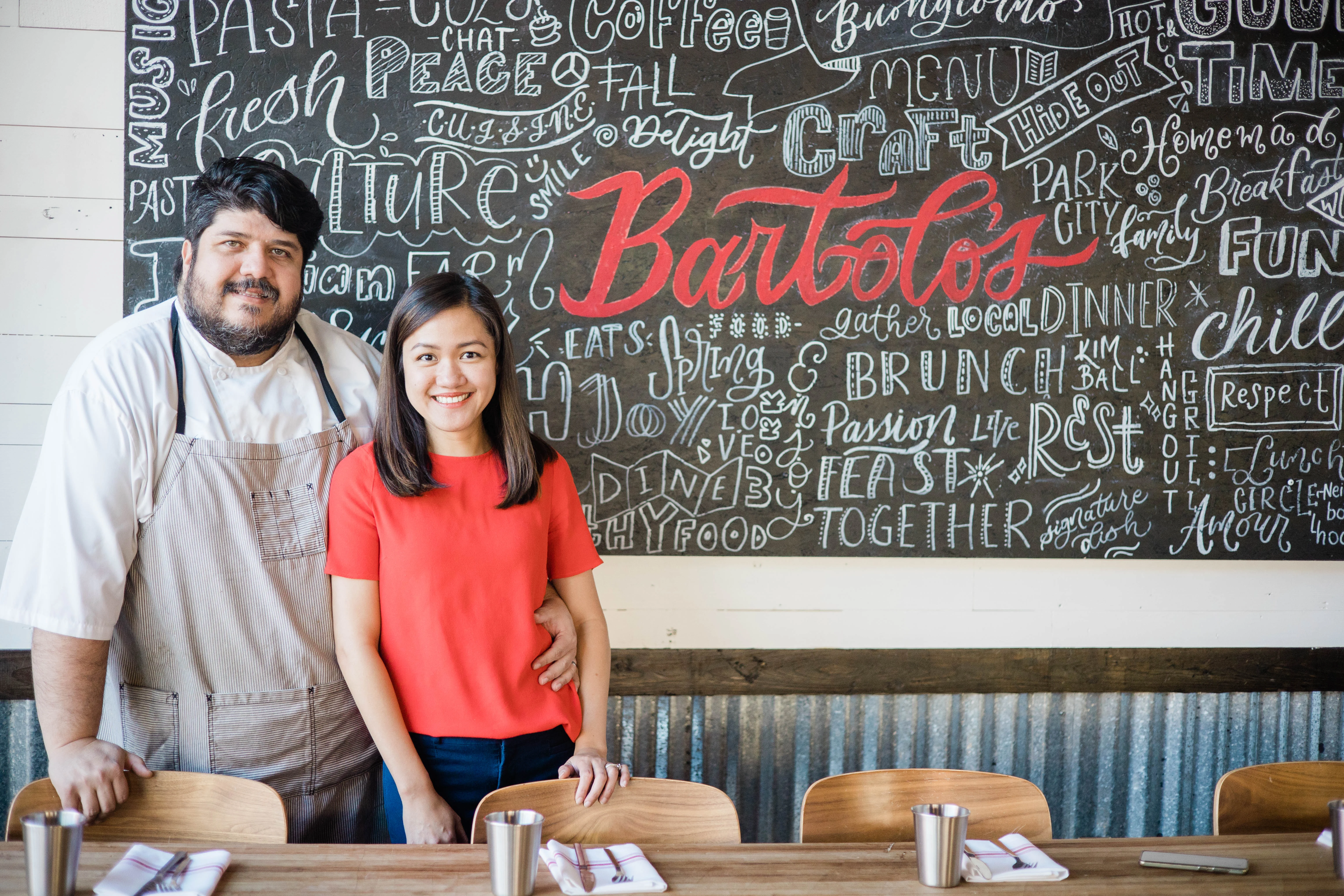 Cozy restaurant owners posing in front of a chalkboard menu